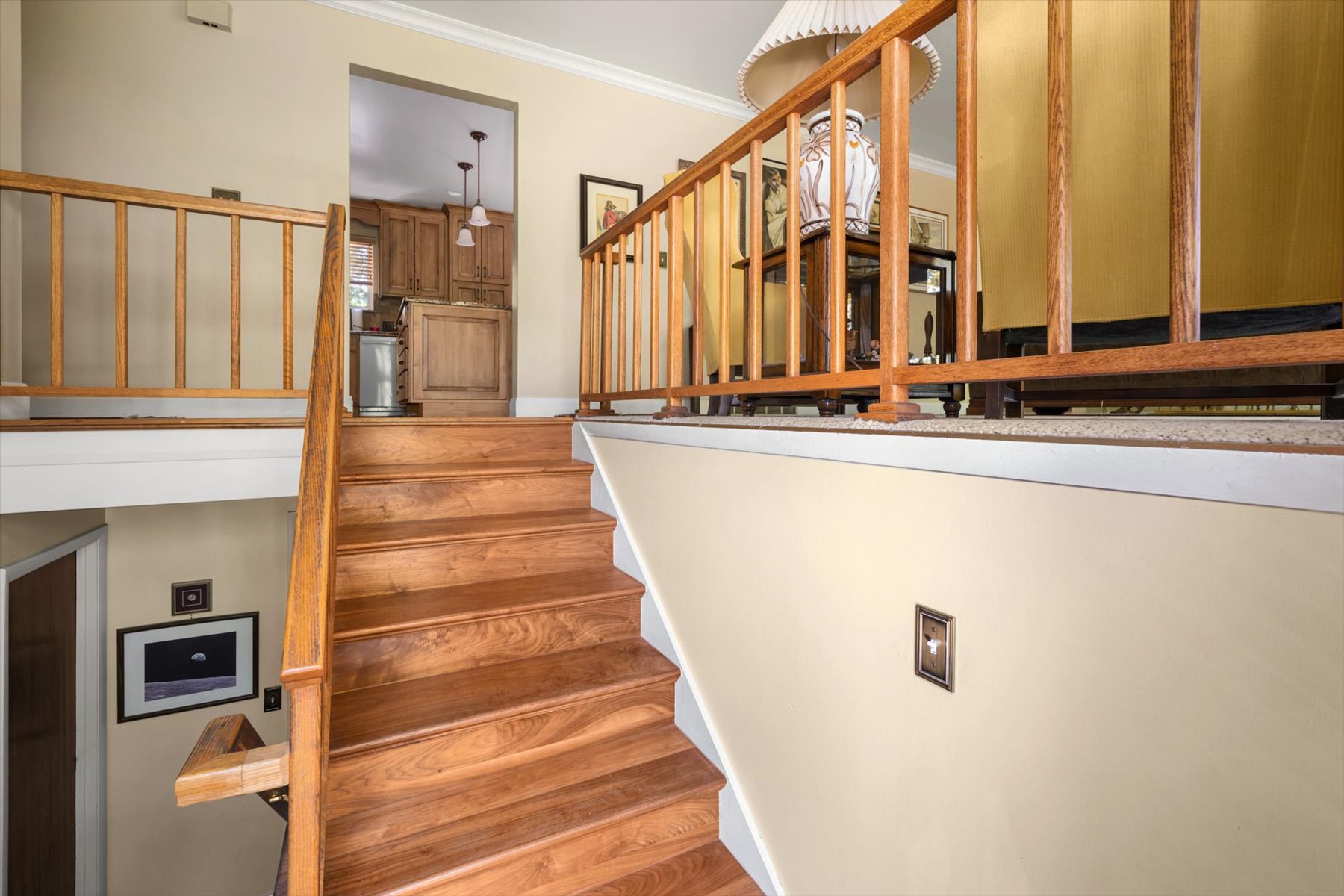 Hardwood staircase with natural wood railings, leading to an upper level with an open doorway to a kitchen featuring wood cabinetry and pendant lighting