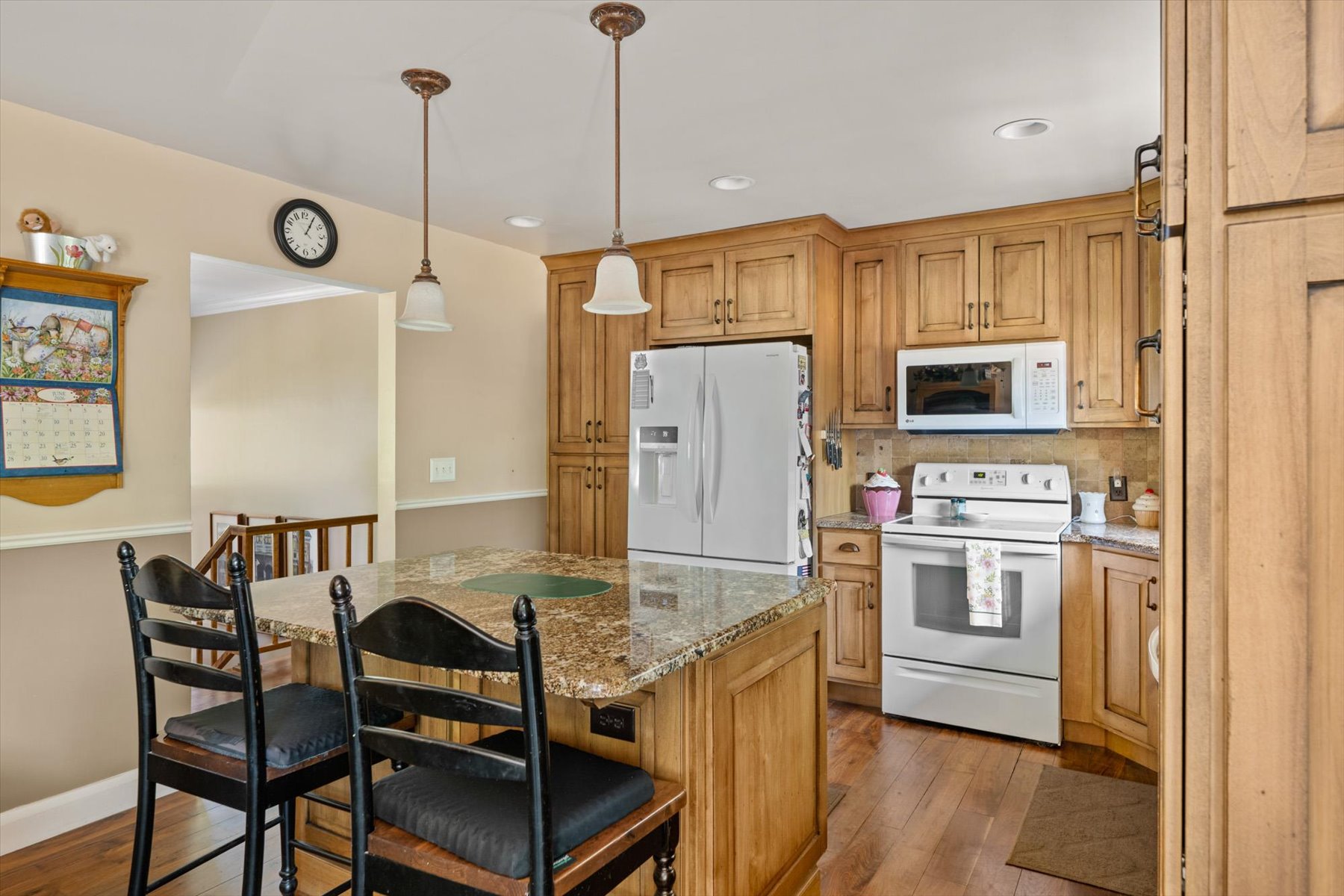 Kitchen featuring warm wood cabinetry, granite countertops, a central island with seating, pendant lighting, and stainless steel appliances