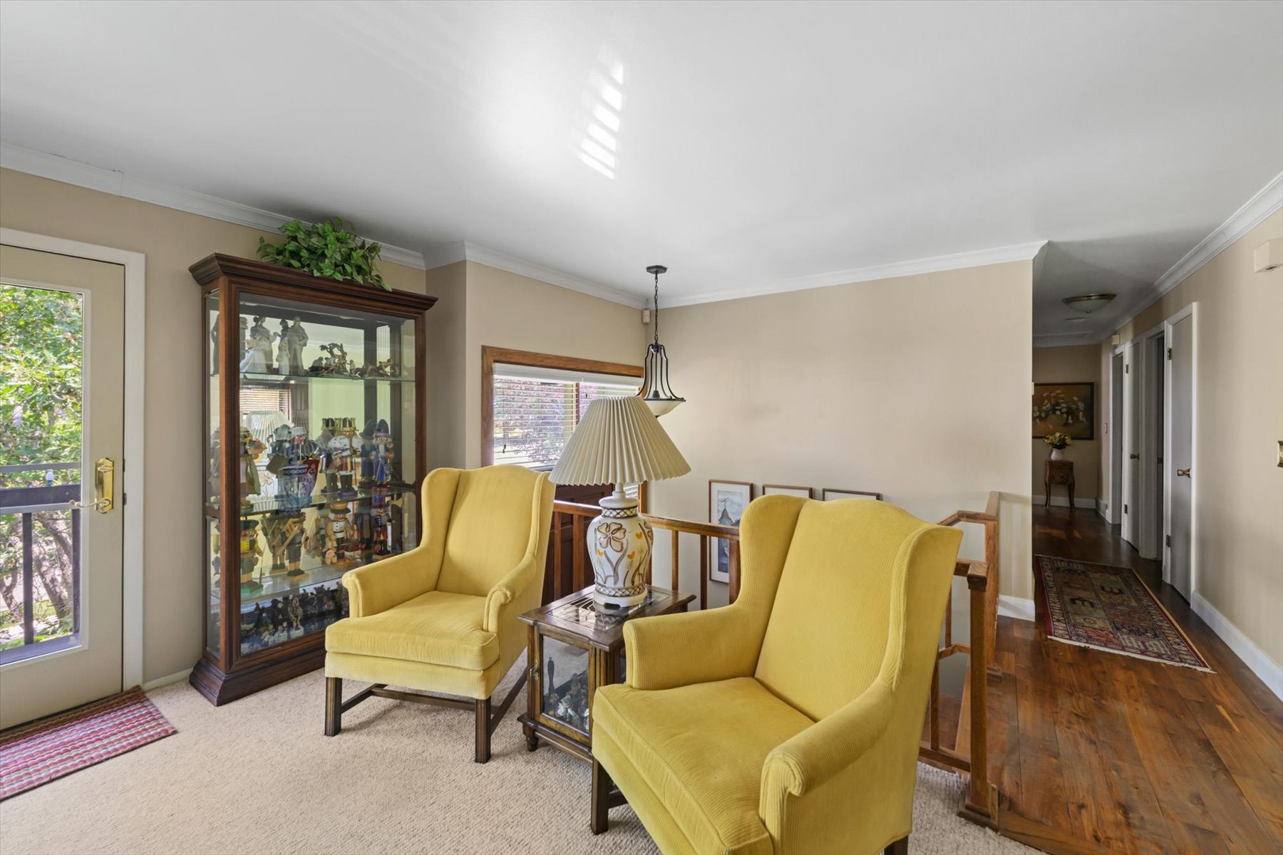 Carpeted landing area featuring a glass-front display cabinet, a glass-paneled door, and wood-finish flooring extending into a hallway