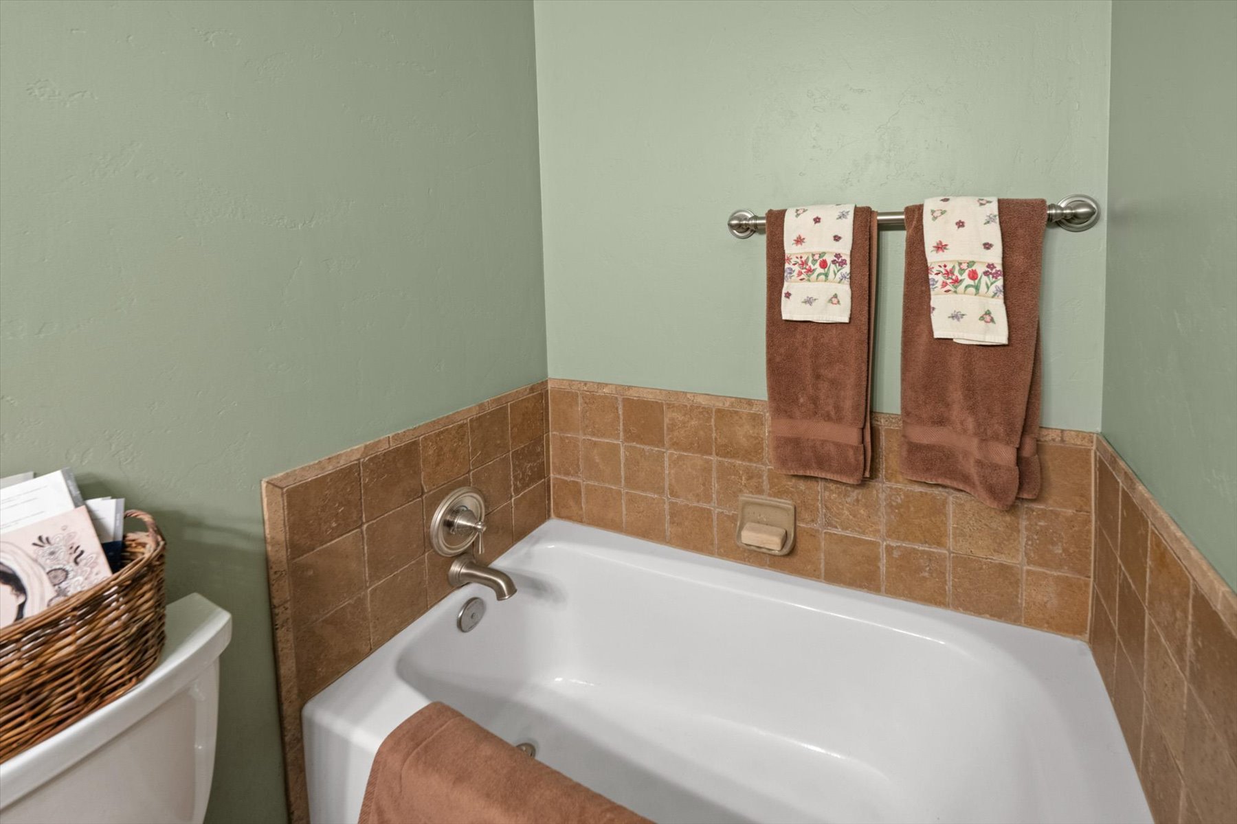 White drop-in bathtub with a brushed nickel faucet and natural stone tile surround