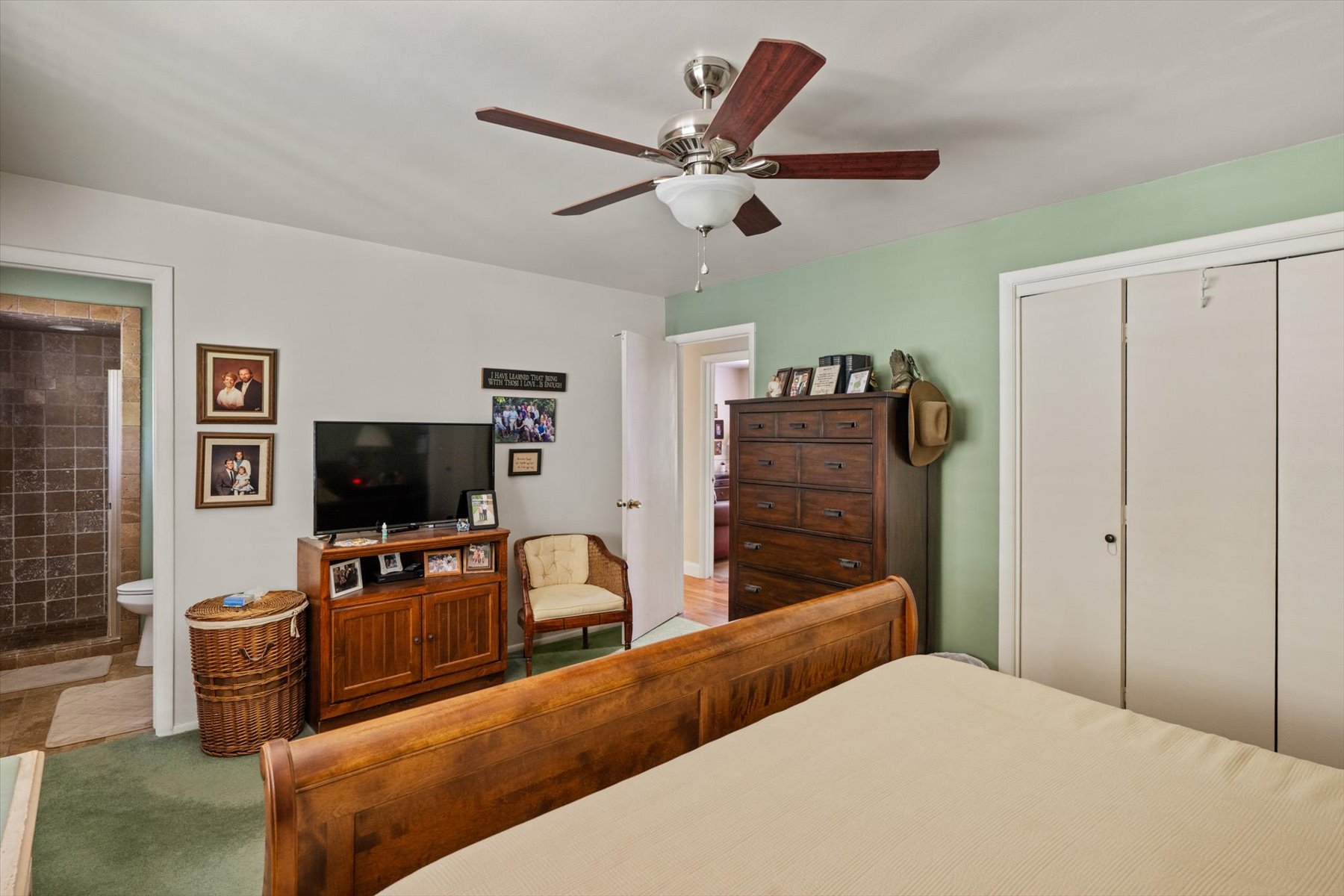 Bedroom featuring a ceiling fan with light fixture, green accent wall, and double-door closet