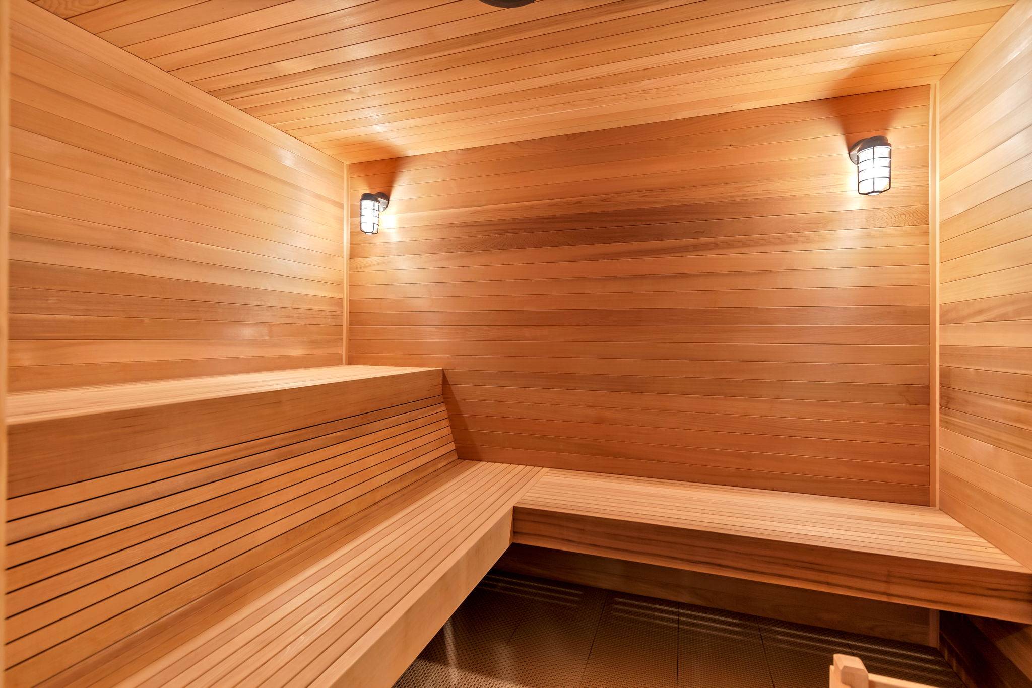 Custom sauna featuring tiered wooden benches, tongue-and-groove wood paneling, and two wall-mounted light fixtures