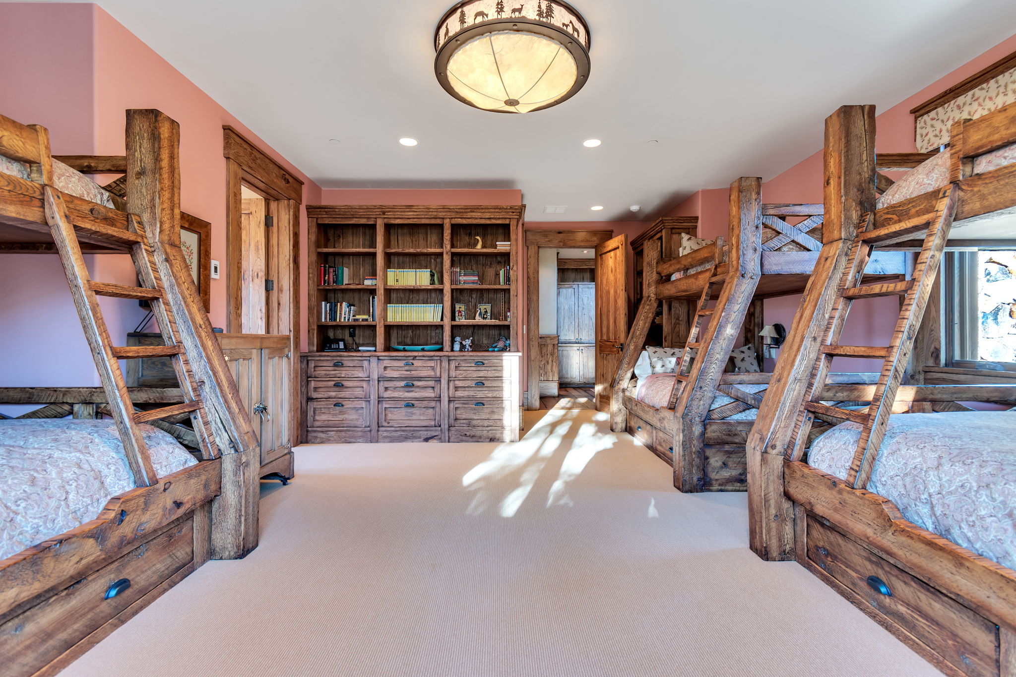 Room featuring light carpeting, built-in wooden bunk beds with storage drawers, a comprehensive built-in wooden bookshelf with lower cabinetry, a rustic wood door frame, and a decorative ceiling light fixture