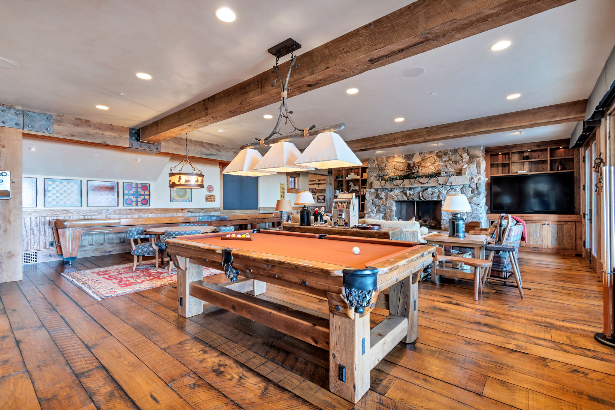 Spacious great room featuring exposed wood beam ceilings, wood-finish flooring, a stone-clad fireplace, and extensive built-in cabinetry