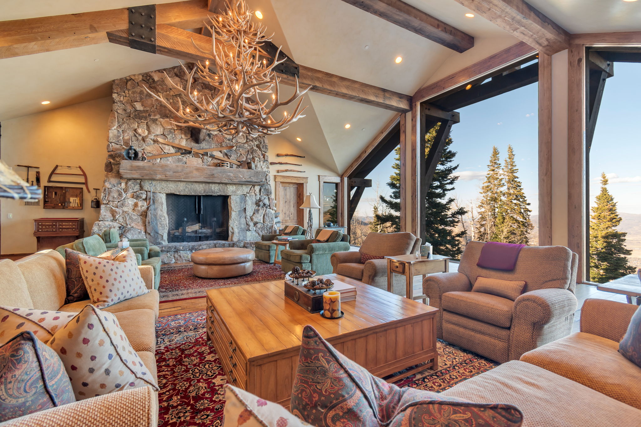 Spacious living area featuring a vaulted ceiling with exposed wood beams, a prominent stone fireplace, large picture windows, recessed lighting, and wood-finish flooring