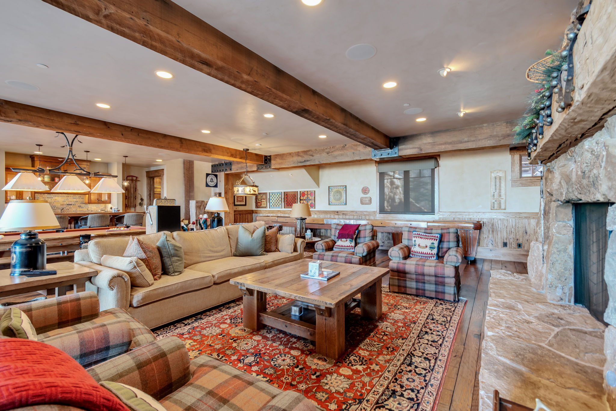 Spacious living area featuring exposed wood beams, recessed lighting, a stone-clad fireplace, wood-finish flooring, and a large area rug