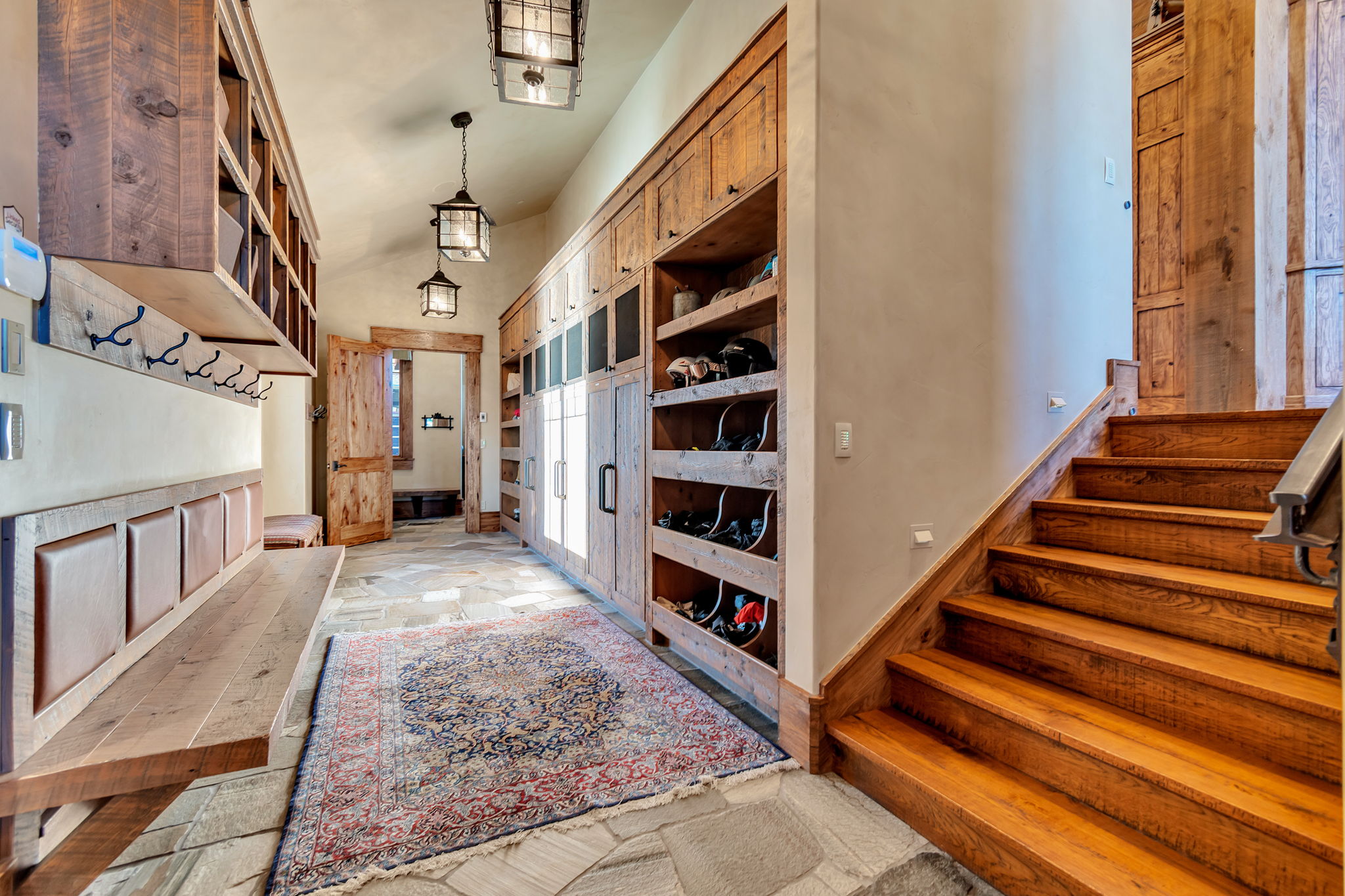 Mudroom featuring stone tile flooring, built-in wooden cabinetry with varied storage, a wooden bench with paneling, and an exposed wood staircase with a metal handrail