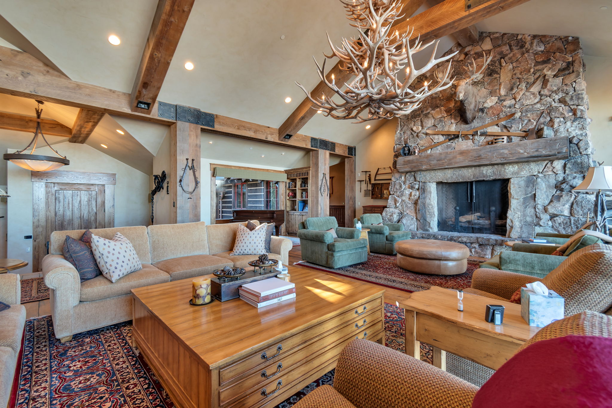 Spacious living area featuring a prominent stone fireplace with a thick wood mantel, vaulted ceilings with exposed wood beams, and recessed lighting