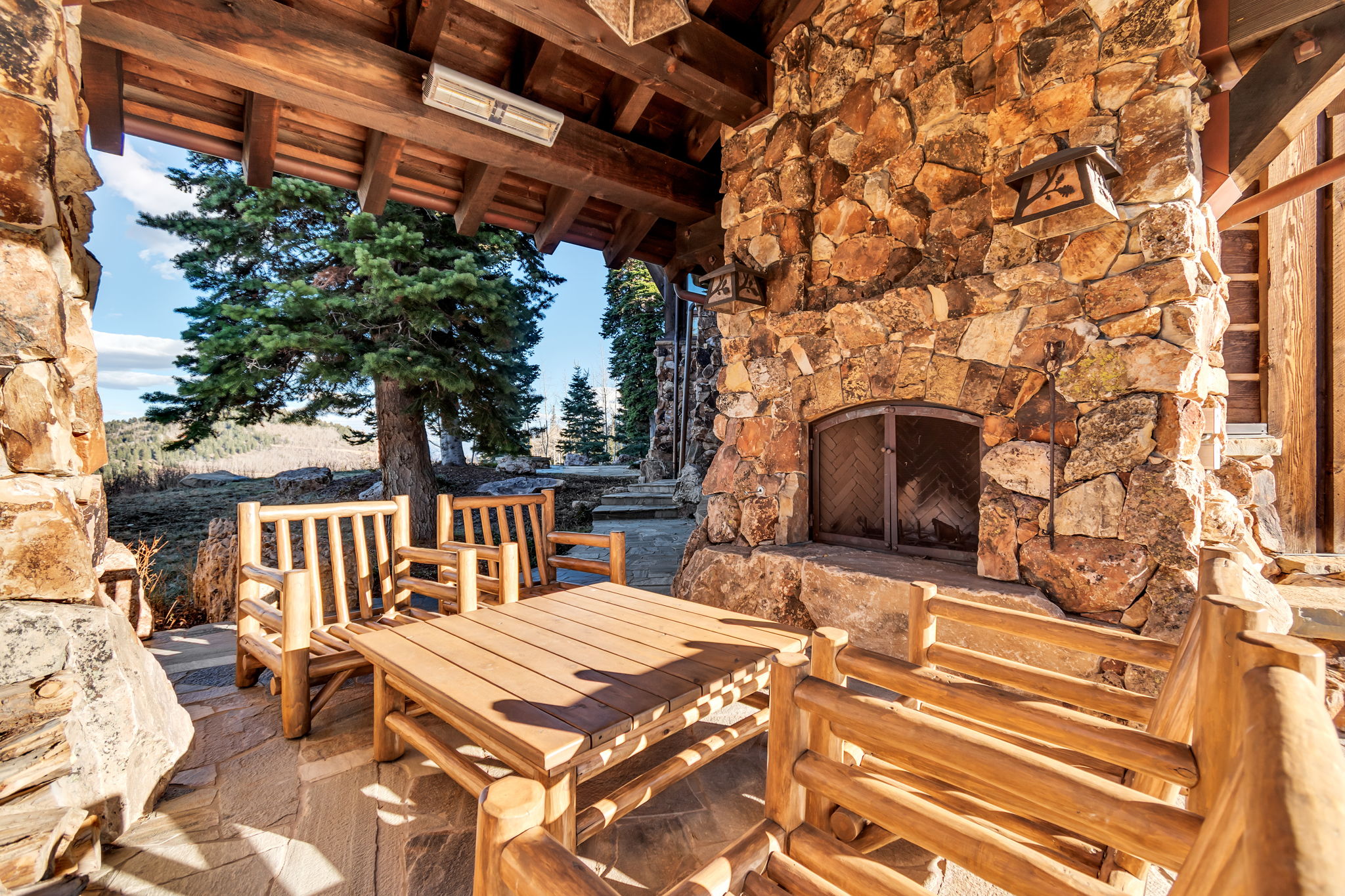 Stone-clad outdoor fireplace with metal grate, set on a flagstone patio