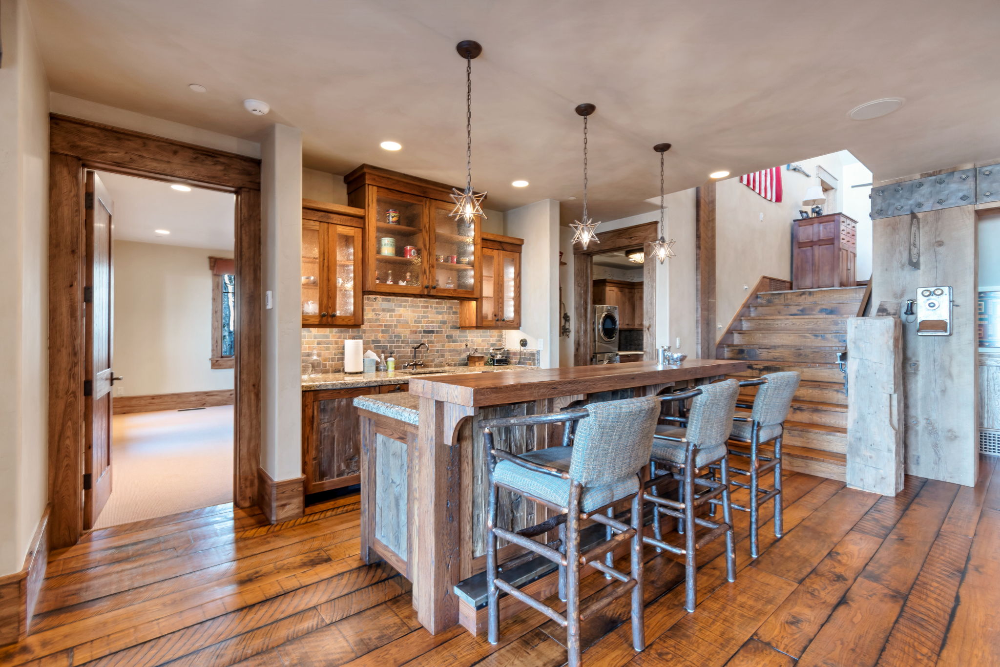 Rustic wood-finish flooring extending into a wet bar area featuring pendant lighting and built-in cabinetry with glass fronts
