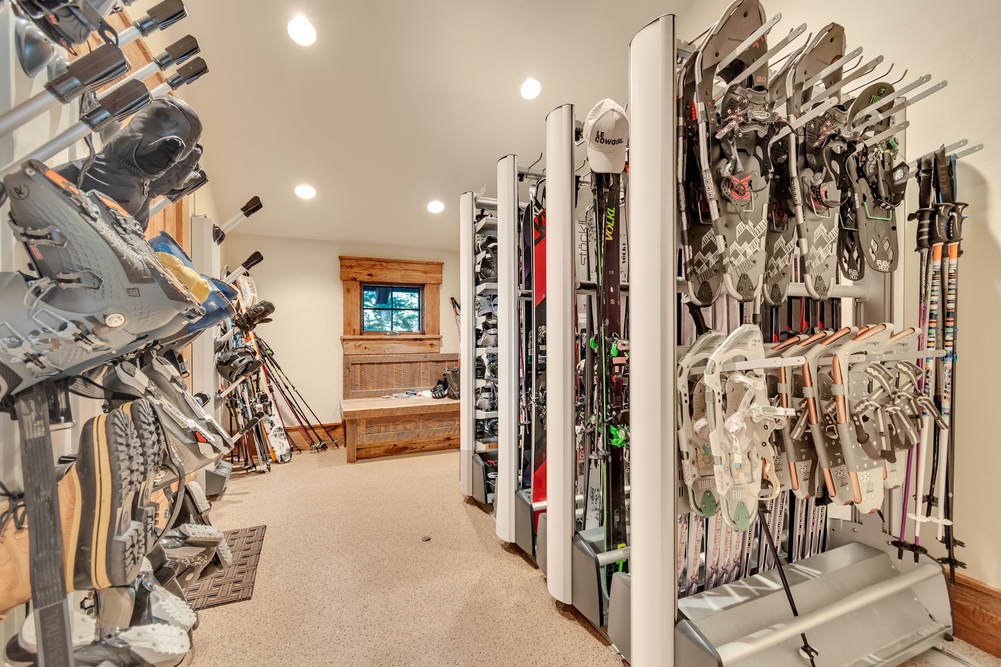 Dedicated gear storage area featuring wall-mounted racks, recessed lighting, and a built-in wooden bench with a window