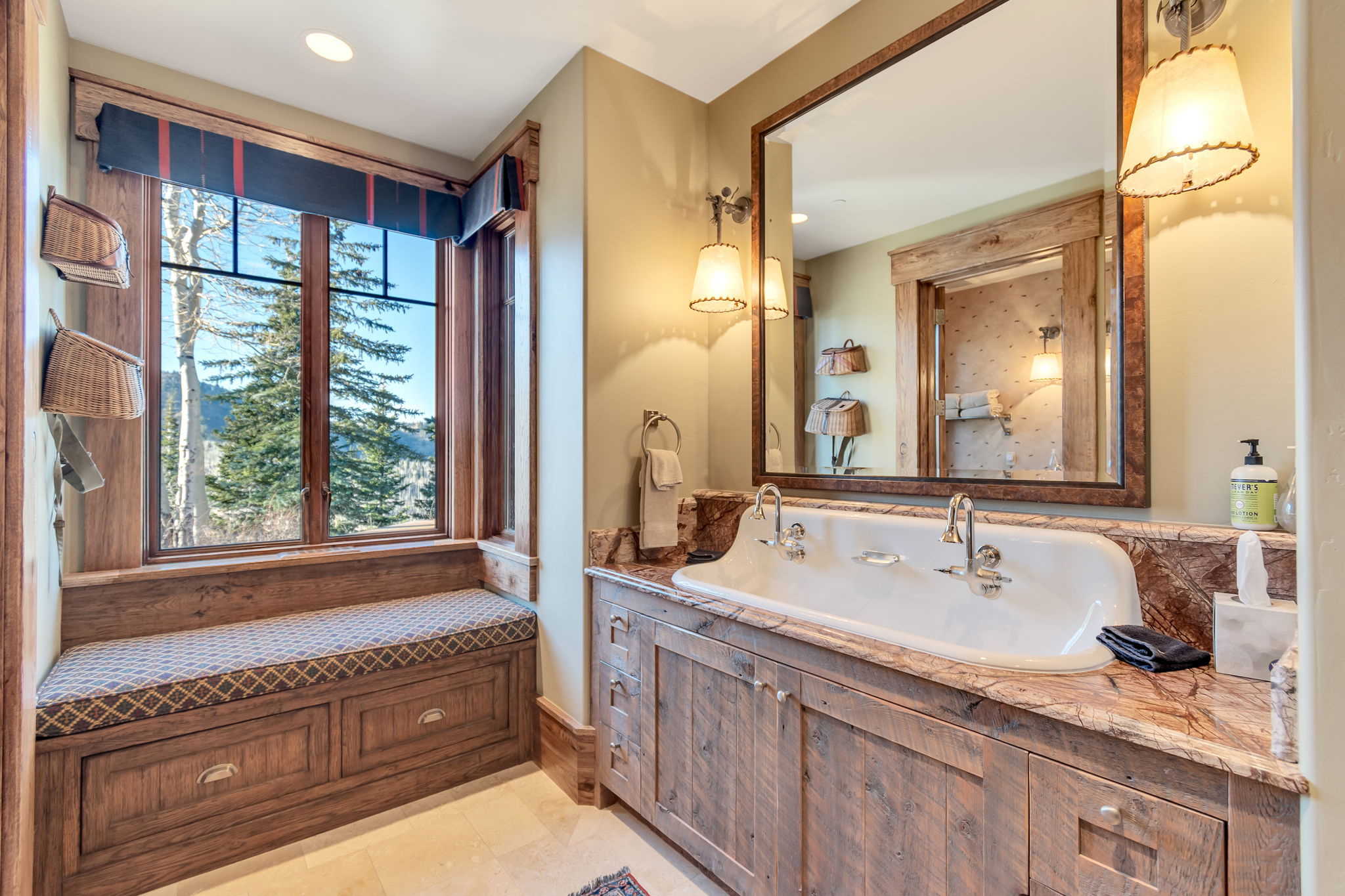 Spacious bathroom featuring a double vanity with a marble countertop, rustic wood-finish cabinetry, a large framed mirror, and two wall-mounted sconces