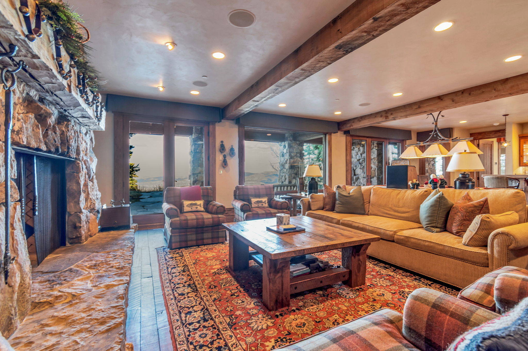 Spacious living area featuring a stone fireplace, exposed wood beams, and large glass doors