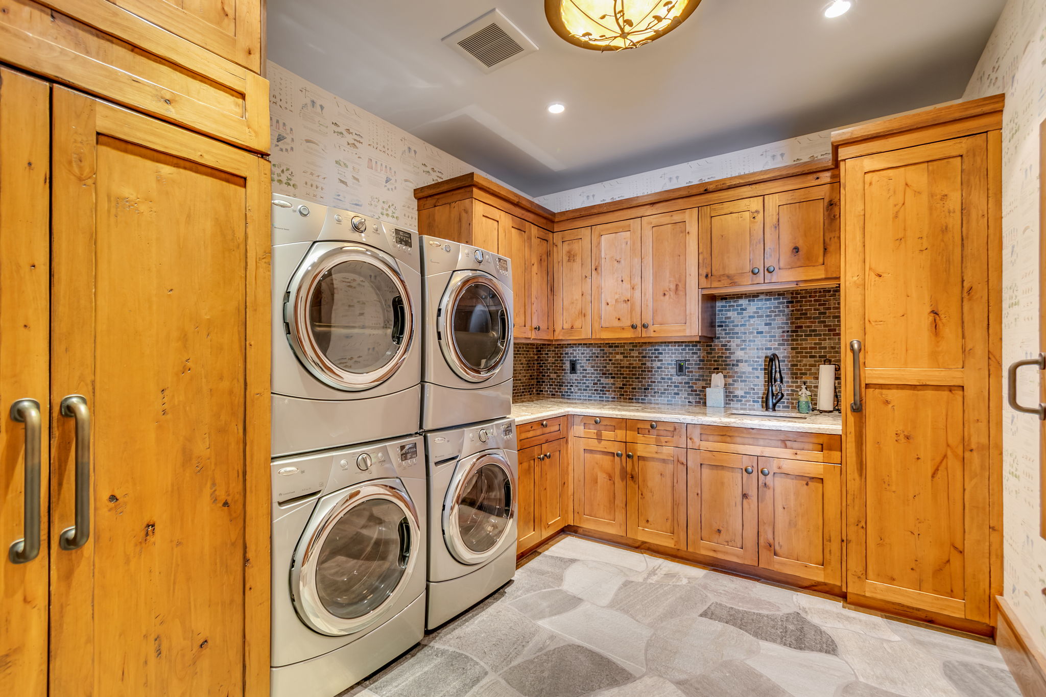 Dedicated utility room featuring two sets of stacked laundry appliances, extensive wood cabinetry, and a countertop with an integrated sink