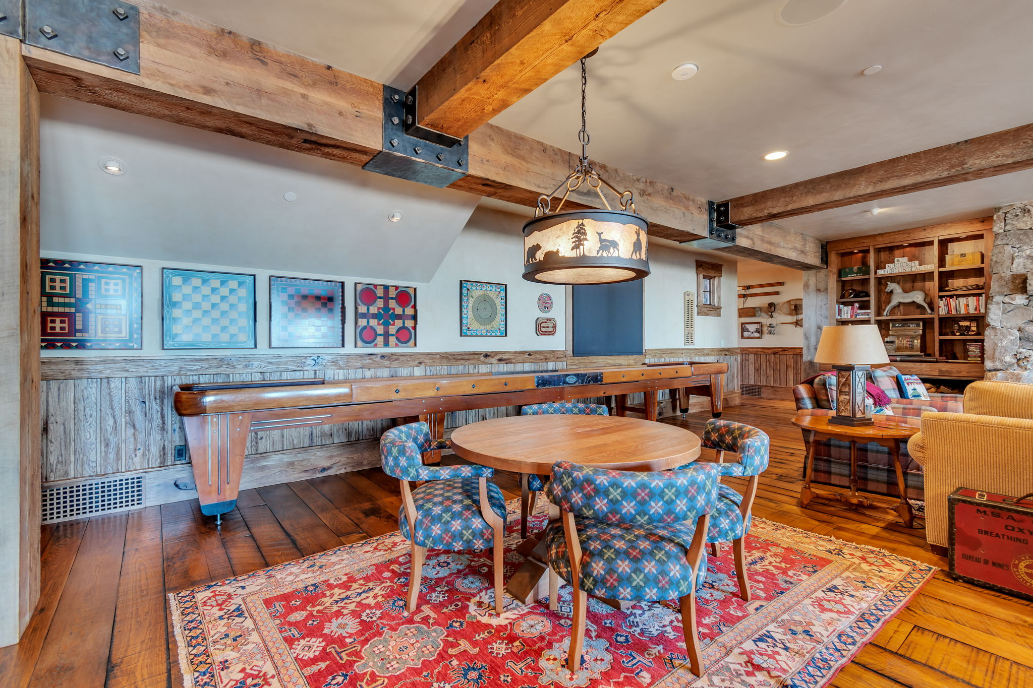 Exposed wood beam ceiling with metal accents, wood-finish flooring, built-in shelving, stone wall detail, and a decorative overhead light fixture