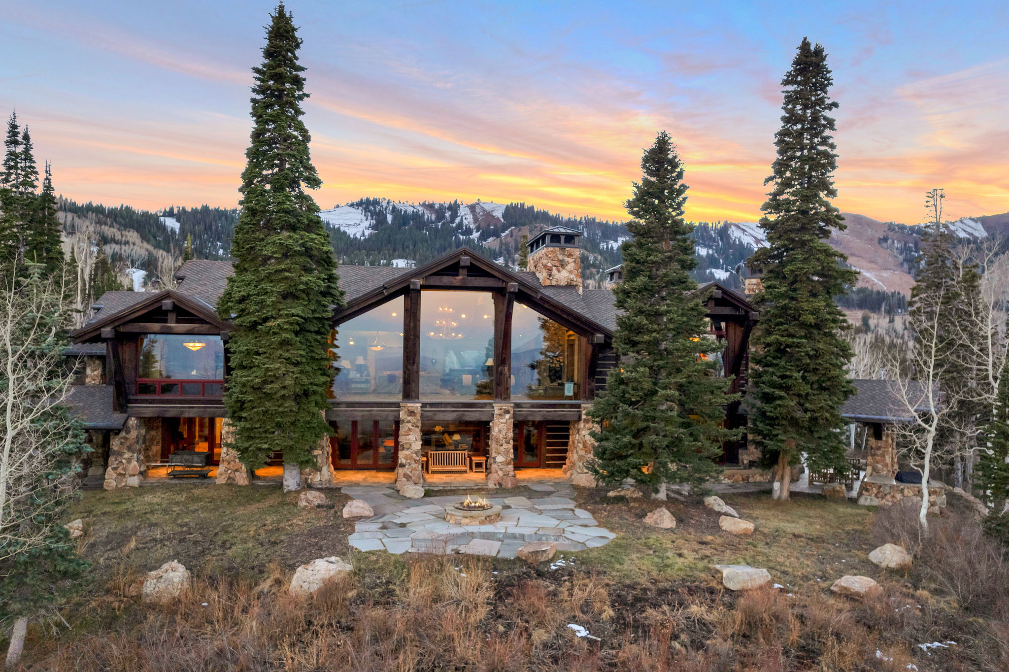Expansive mountain lodge-style residence featuring a stone and wood exterior with a prominent A-frame window wall