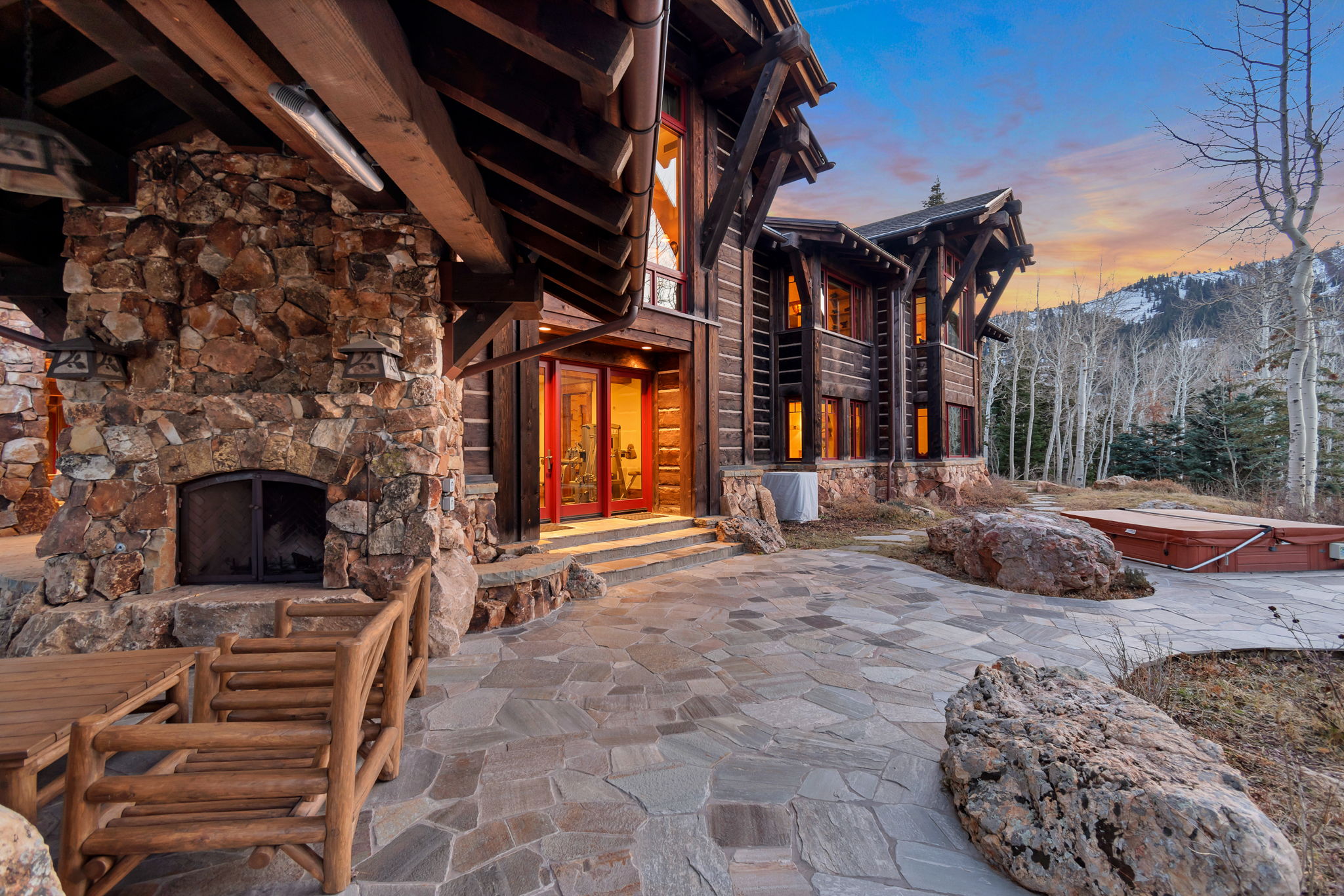 Stone patio featuring an outdoor fireplace with natural stone surround and a covered hot tub