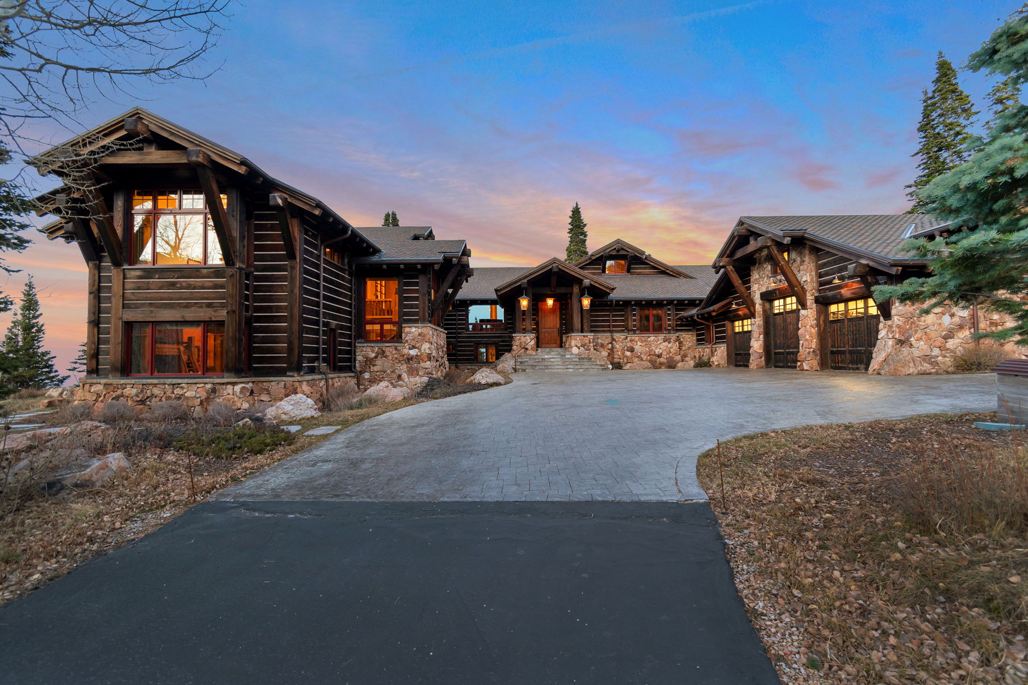 Expansive log and stone residence featuring a multi-car garage, prominent gables, large picture windows, and a stone foundation