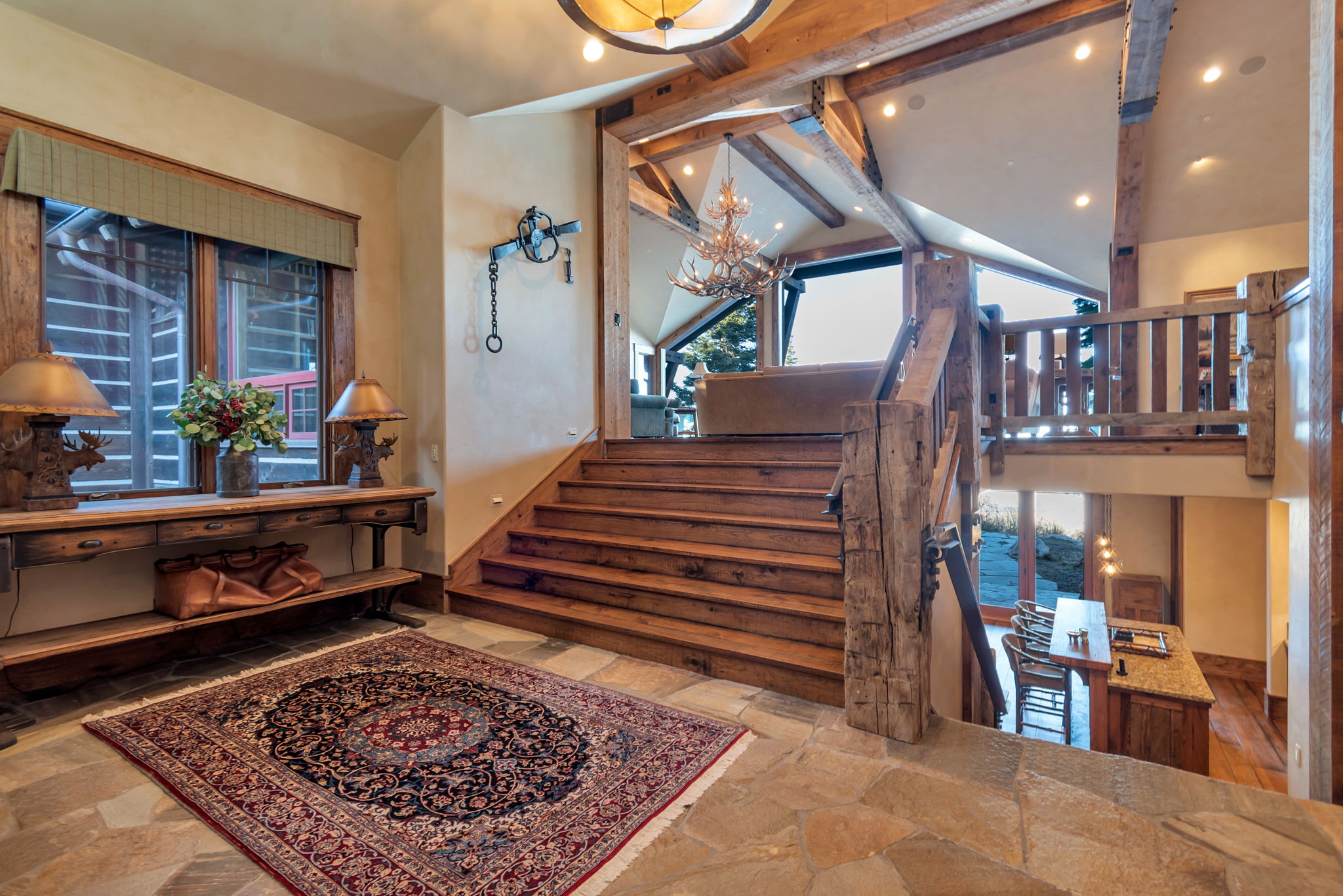 Stone tile flooring in a multi-level interior featuring exposed wood beams and a rustic wood staircase