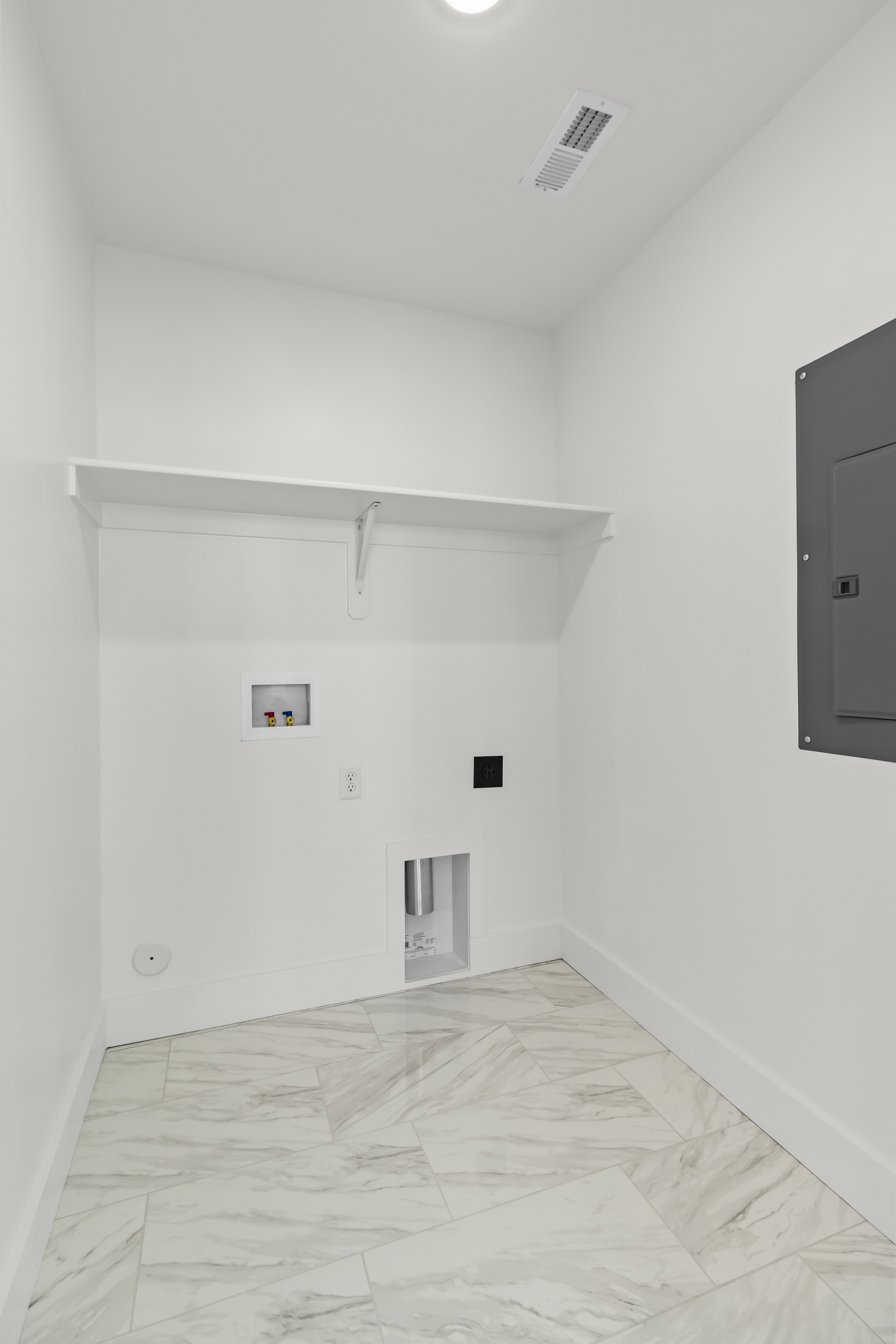 Utility room with white walls, a white storage shelf, and light-toned tile flooring