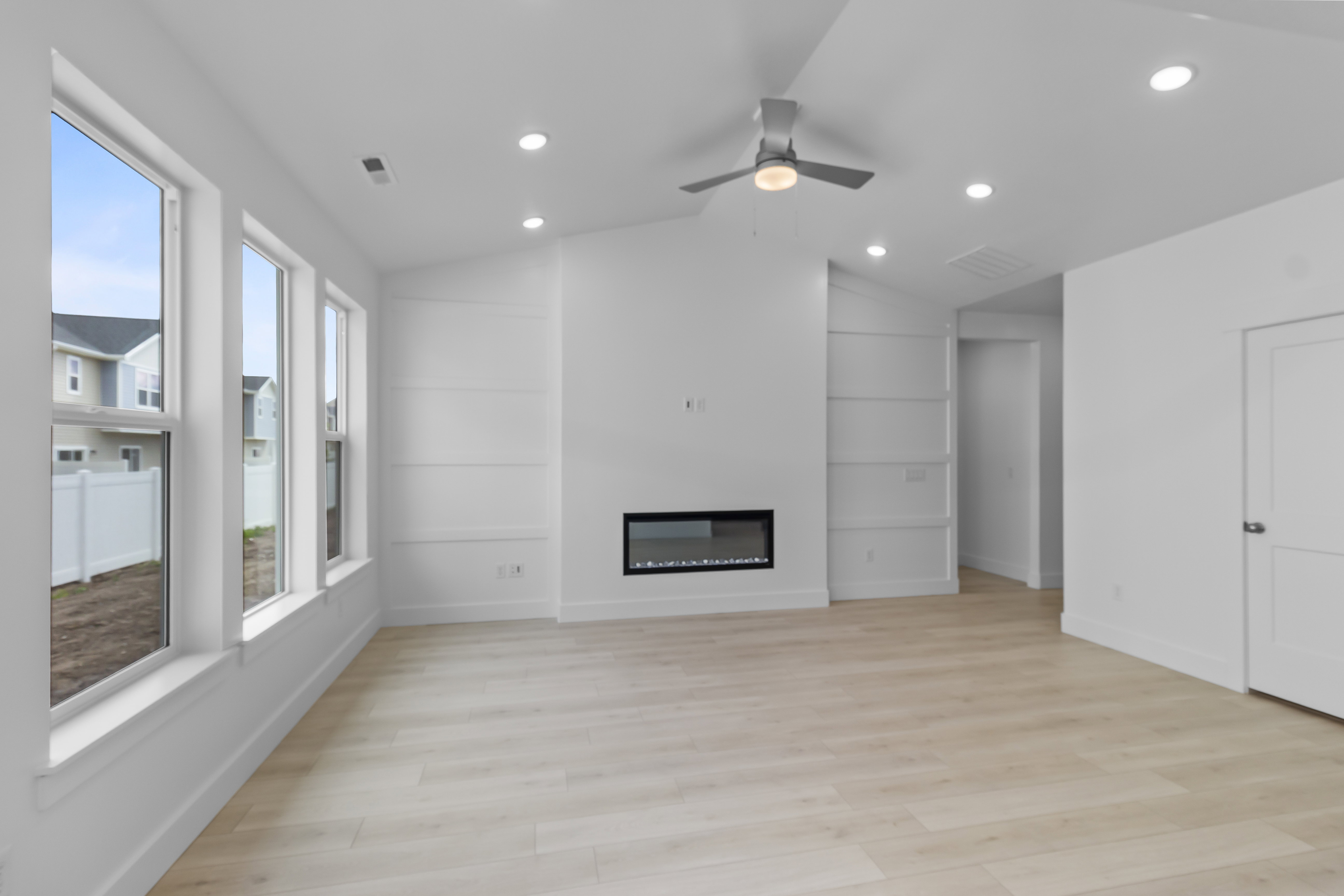 Living area featuring multiple large windows, light wood-finish flooring, recessed lighting, and a modern linear electric fireplace