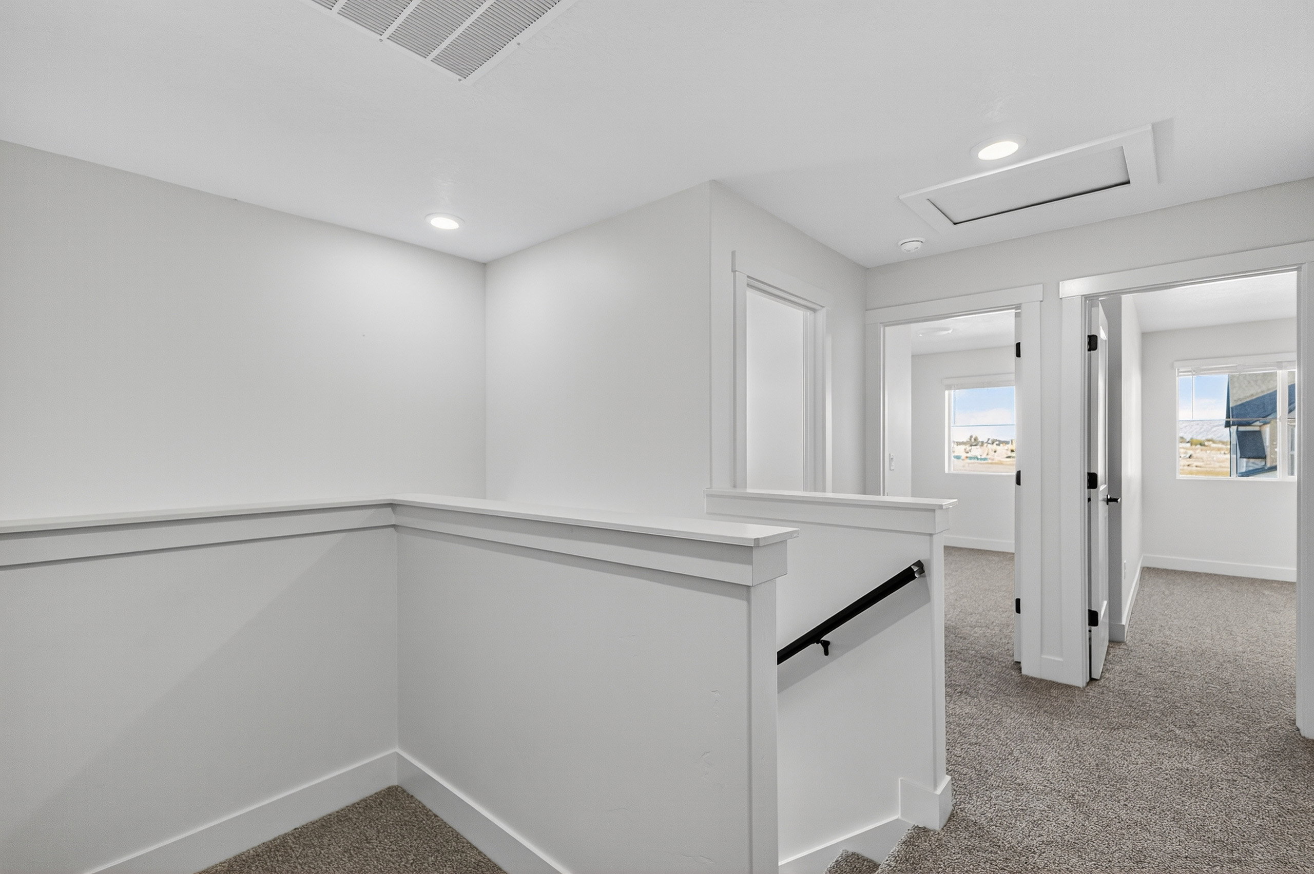 Carpeted landing featuring white walls, recessed lighting, white baseboards, and a white railing with a black handrail
