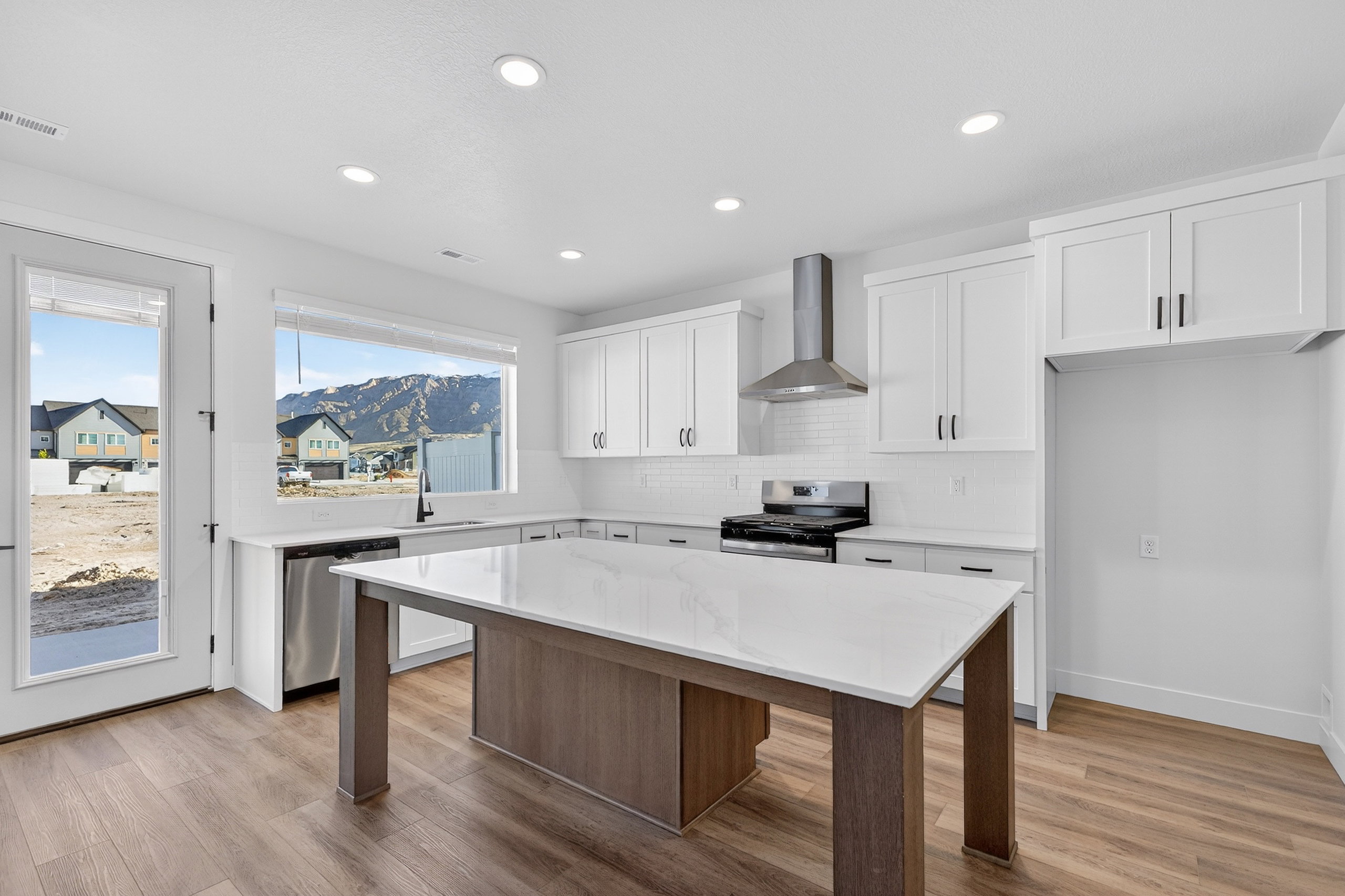 Modern kitchen featuring white shaker cabinetry, stainless steel appliances, a center island with a light-toned countertop, and wood-finish flooring