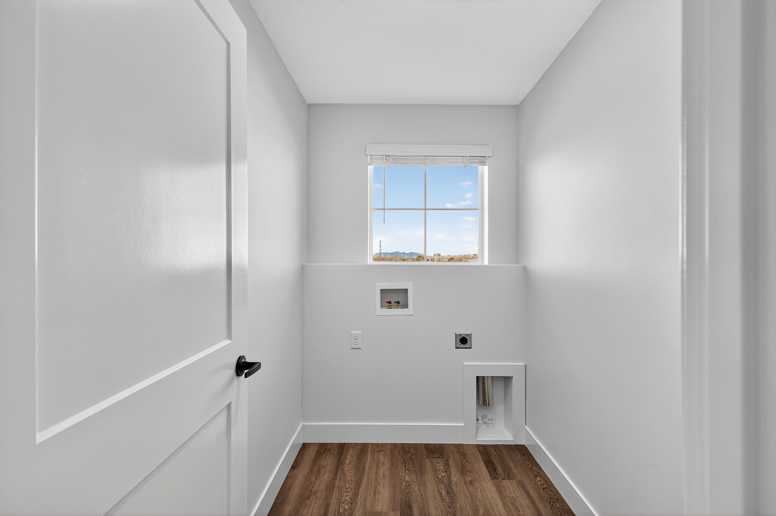 Dedicated utility area featuring wood-finish flooring, crisp white walls, and a window with blinds