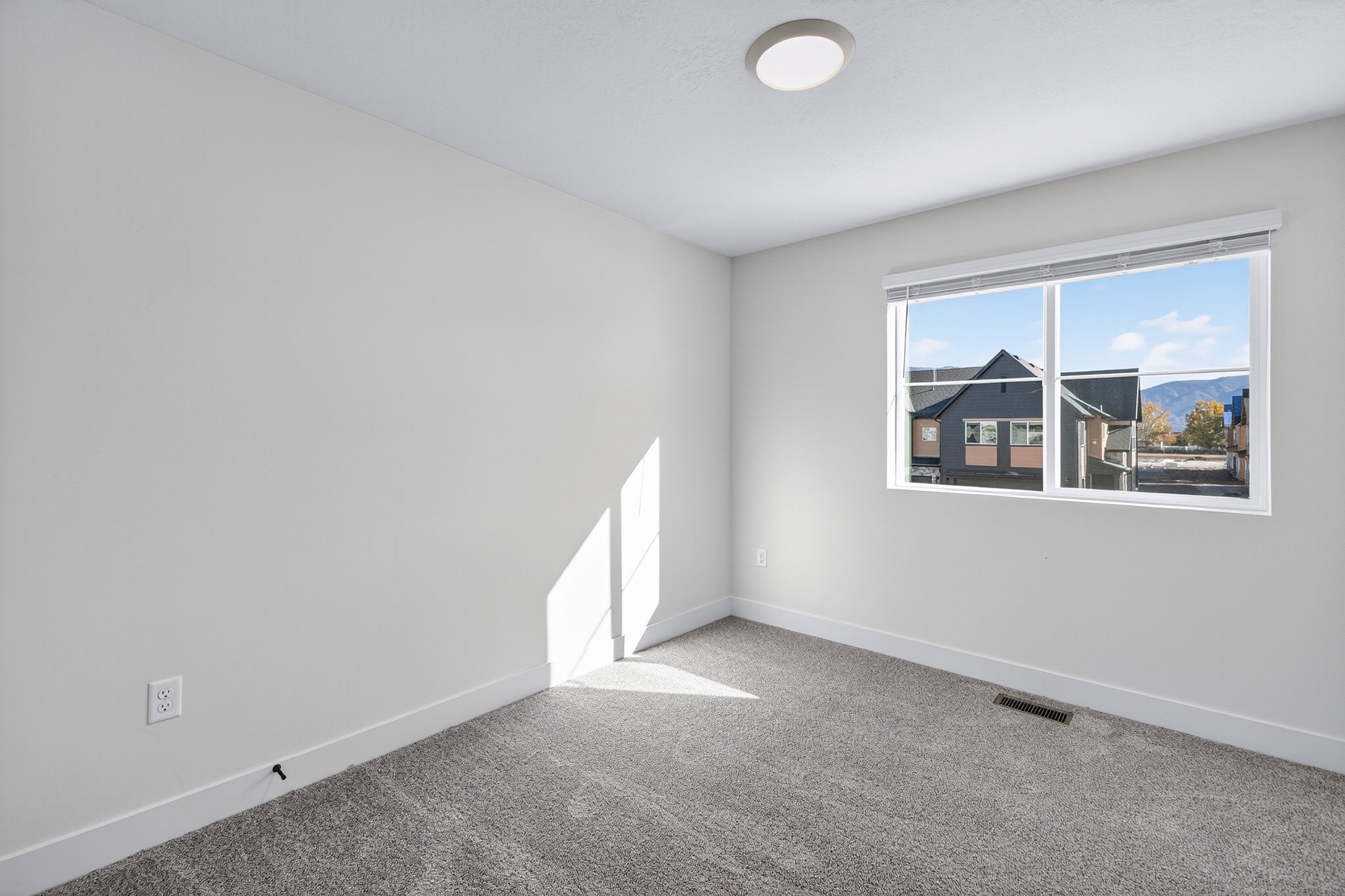 Bright room with neutral wall paint, gray carpet flooring, white baseboards, and a window with mountain scenery
