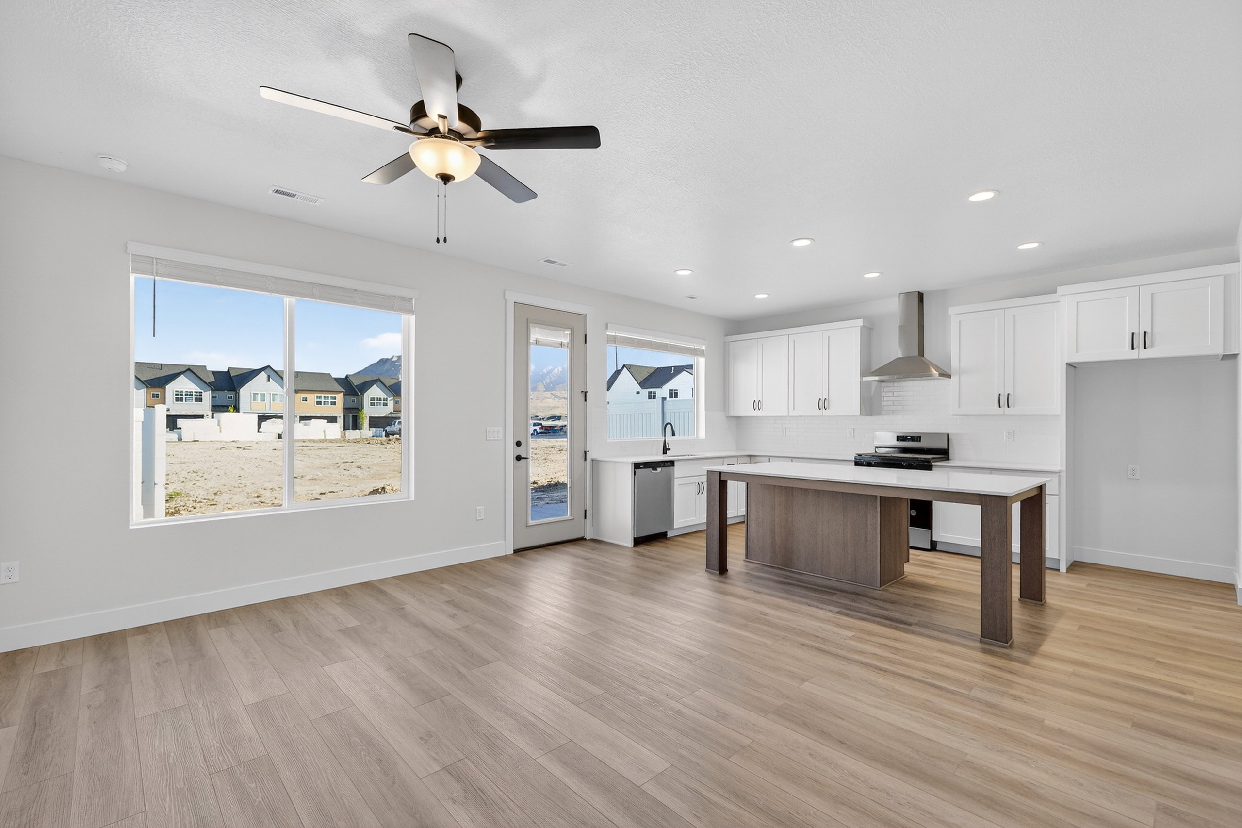 Open-concept living area with wood-finish flooring, a contemporary ceiling fan, and large windows