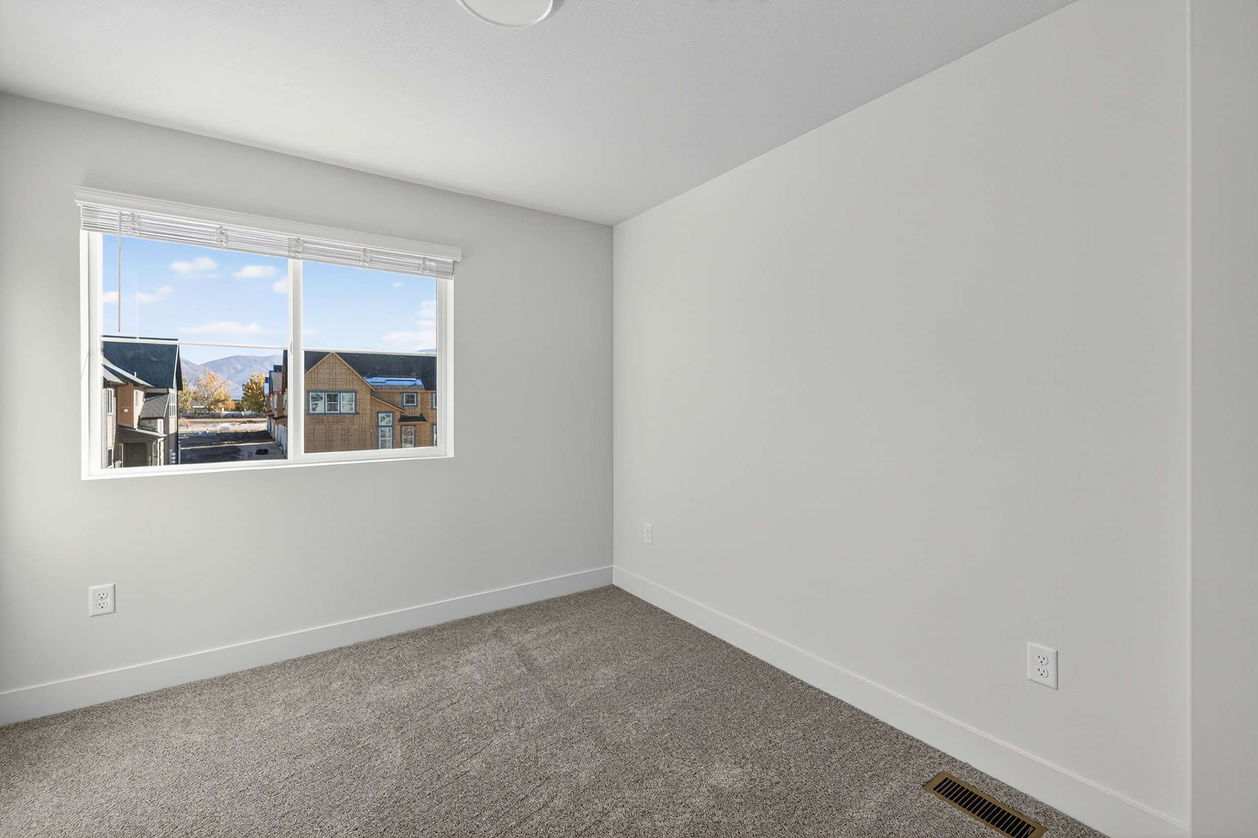 Bright room featuring a large window with white blinds, neutral carpeting, and white baseboards