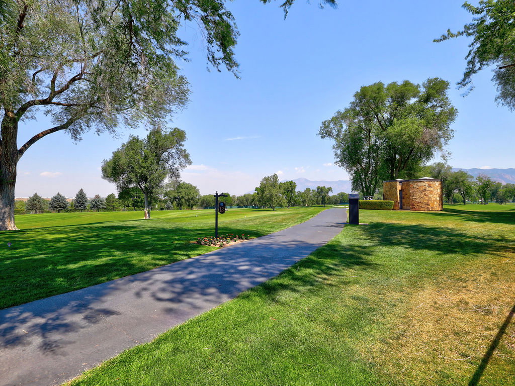 Expansive green space featuring a paved pathway, mature trees, and a stone-clad circular structure