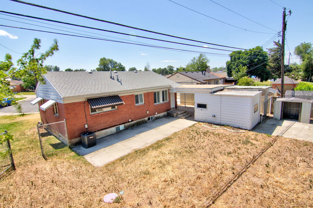 Brick exterior featuring a gray shingle roof, dark window awnings, and an attached white structure with a flat roof