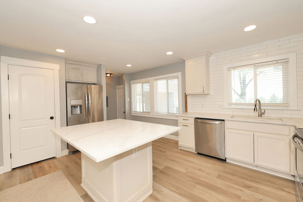 Kitchen featuring a central island with a light-toned countertop, wood-finish flooring, white cabinetry, stainless steel appliances, and a white subway tile backsplash
