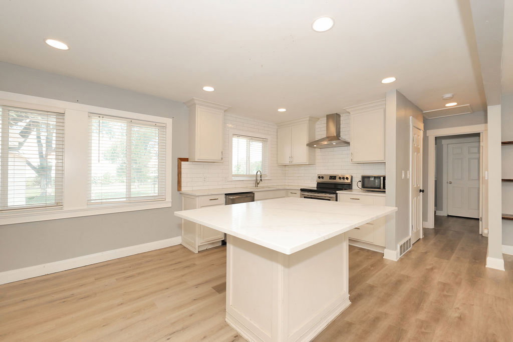 Kitchen featuring a central island with a light-toned countertop, white cabinetry, a subway tile backsplash, stainless steel appliances, and wood-finish flooring