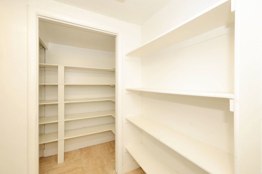 Spacious pantry featuring extensive white shelving and light-toned tile flooring