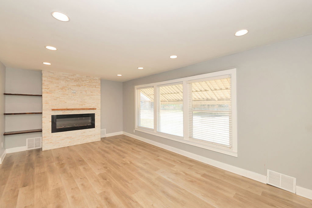Living area featuring a stone-clad fireplace with a wood mantle, an integrated electric firebox, wood-finish flooring, recessed lighting, and built-in shelving