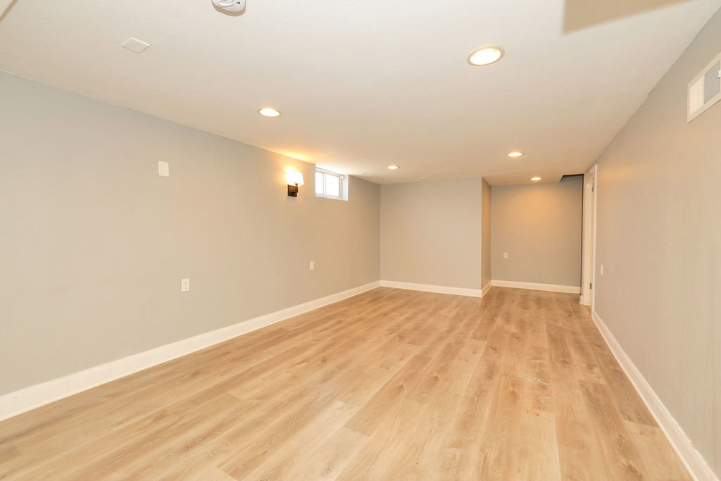 Open room featuring wood-finish flooring, recessed ceiling lights, a wall sconce, and a transom window
