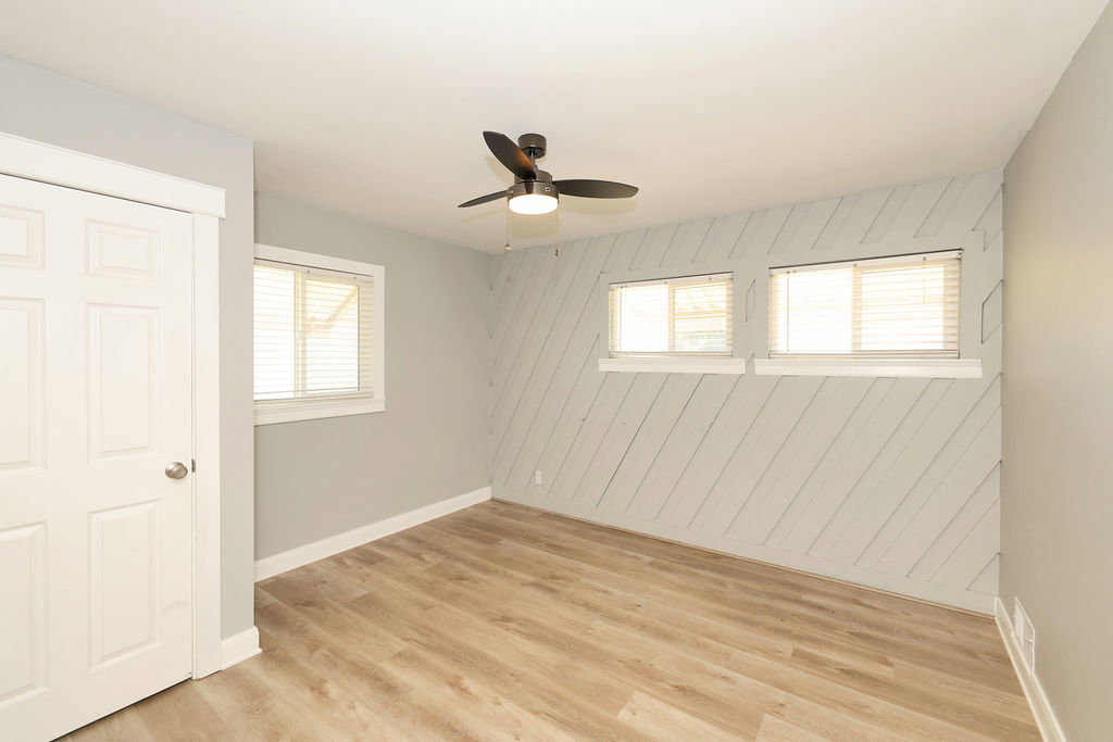 Room featuring wood-finish flooring, a contemporary ceiling fan with integrated lighting, and a distinctive accent wall with angled paneling