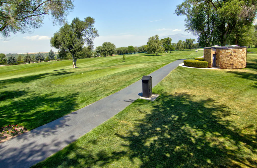 Expansive green space featuring a paved pathway, mature trees, and a stone-clad circular structure