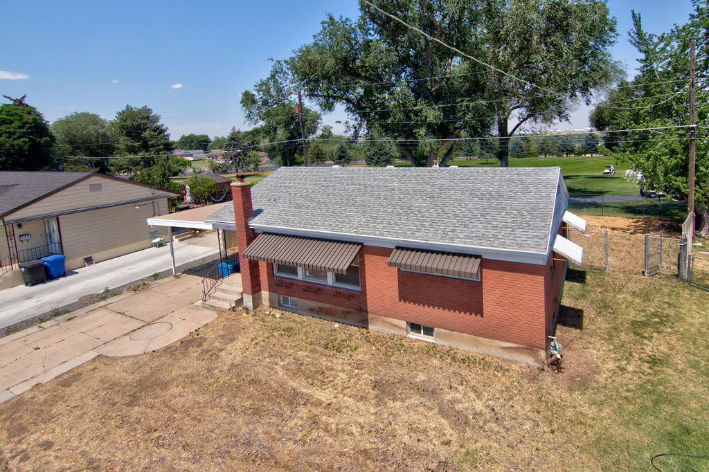 Brick exterior with a gray shingle roof, featuring awning-covered windows, a carport, and a stone chimney