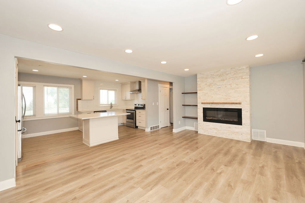 Spacious living area featuring wood-finish flooring, recessed lighting, and a modern electric fireplace with a stone surround