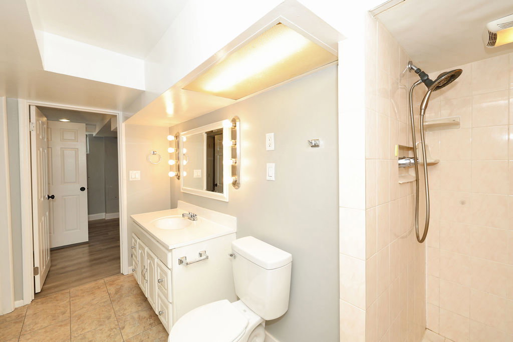 Bathroom featuring a tiled shower, white vanity with integrated sink, Hollywood-style vanity mirror, white toilet, and tile flooring