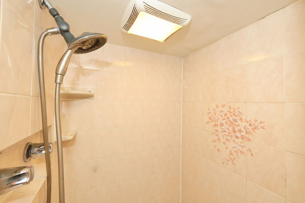 Shower enclosure featuring neutral-toned wall tiling, an integrated wall-mounted shower head, and a ceiling-mounted light fixture with exhaust fan