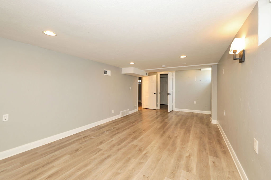 Spacious room featuring wood-finish flooring, recessed ceiling lighting, and a wall-mounted sconce
