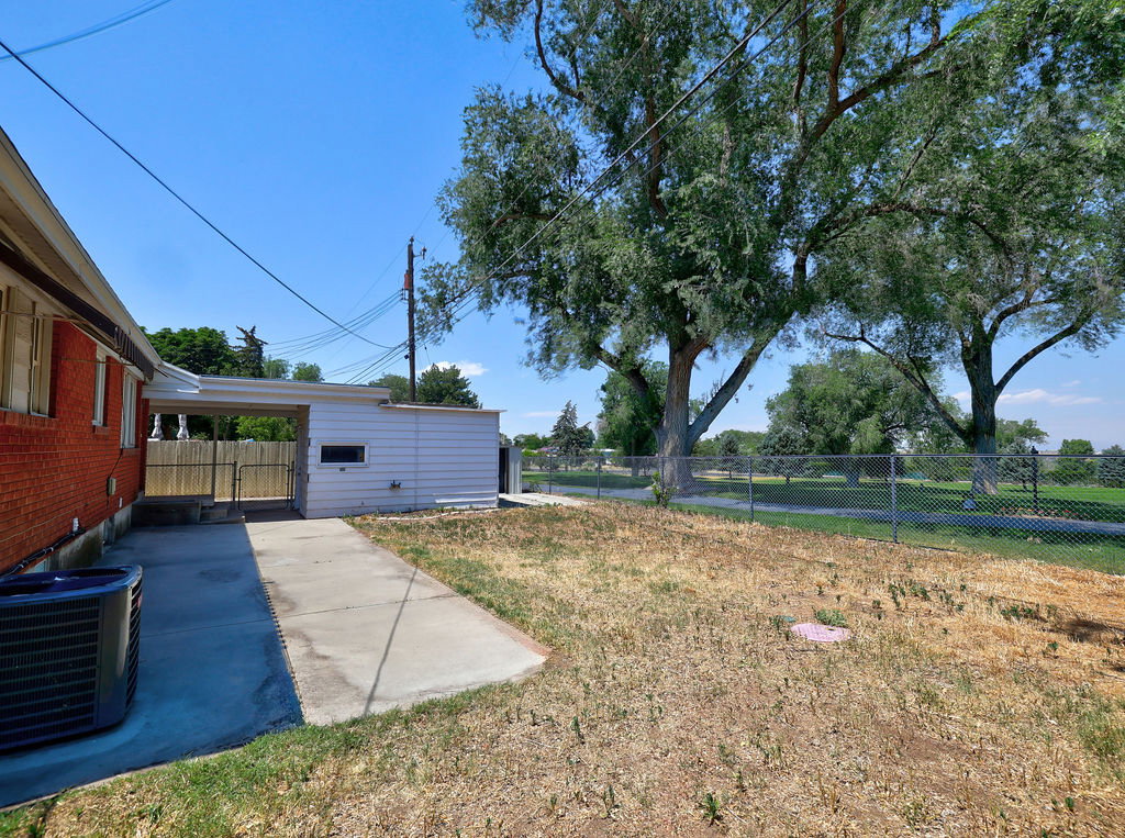 Expansive backyard with mature trees, a chain-link fence, and an extended concrete patio