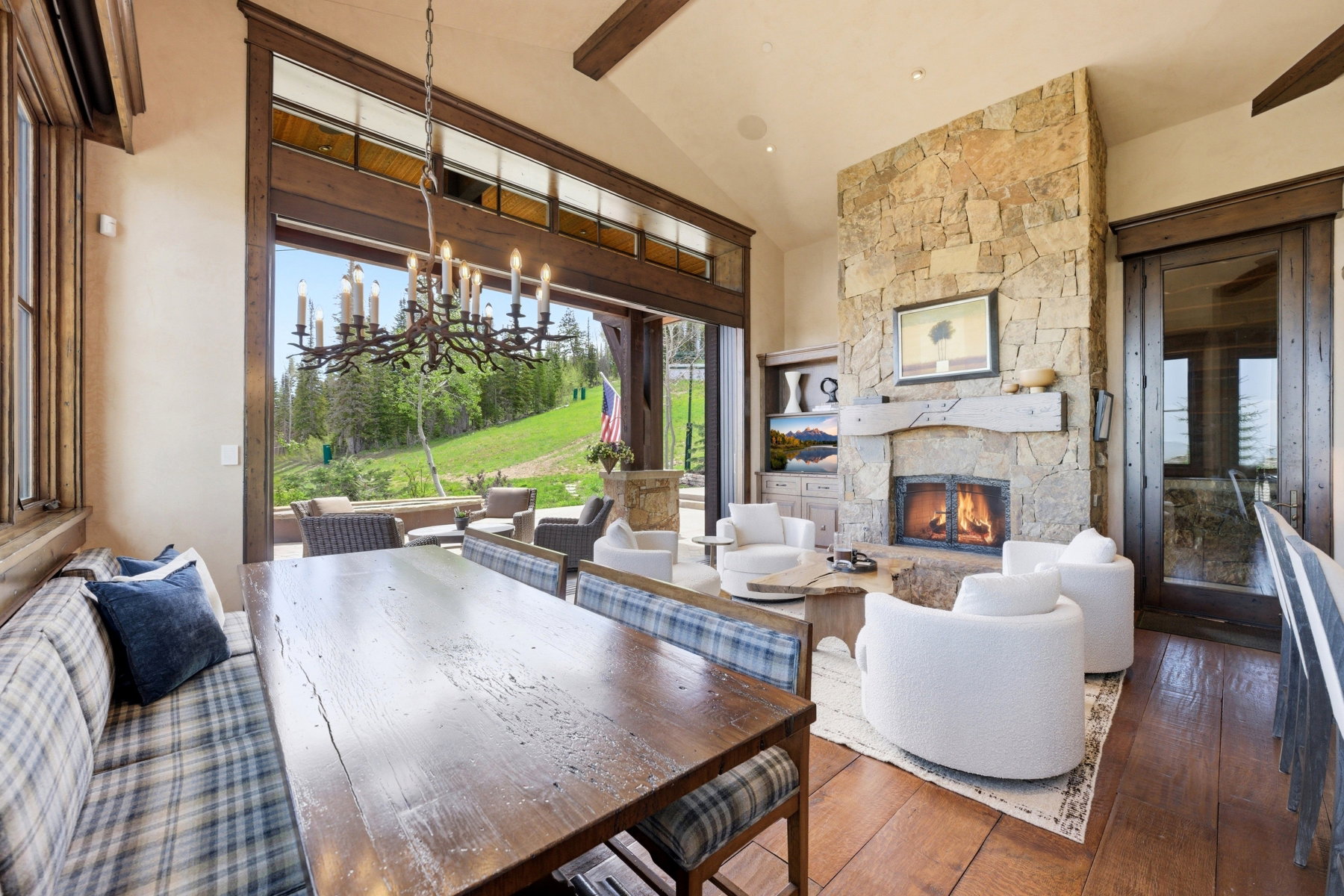 Spacious interior featuring a stone fireplace, wood-finish flooring, vaulted ceilings, a built-in banquette, and a large multi-panel glass door opening to an outdoor patio