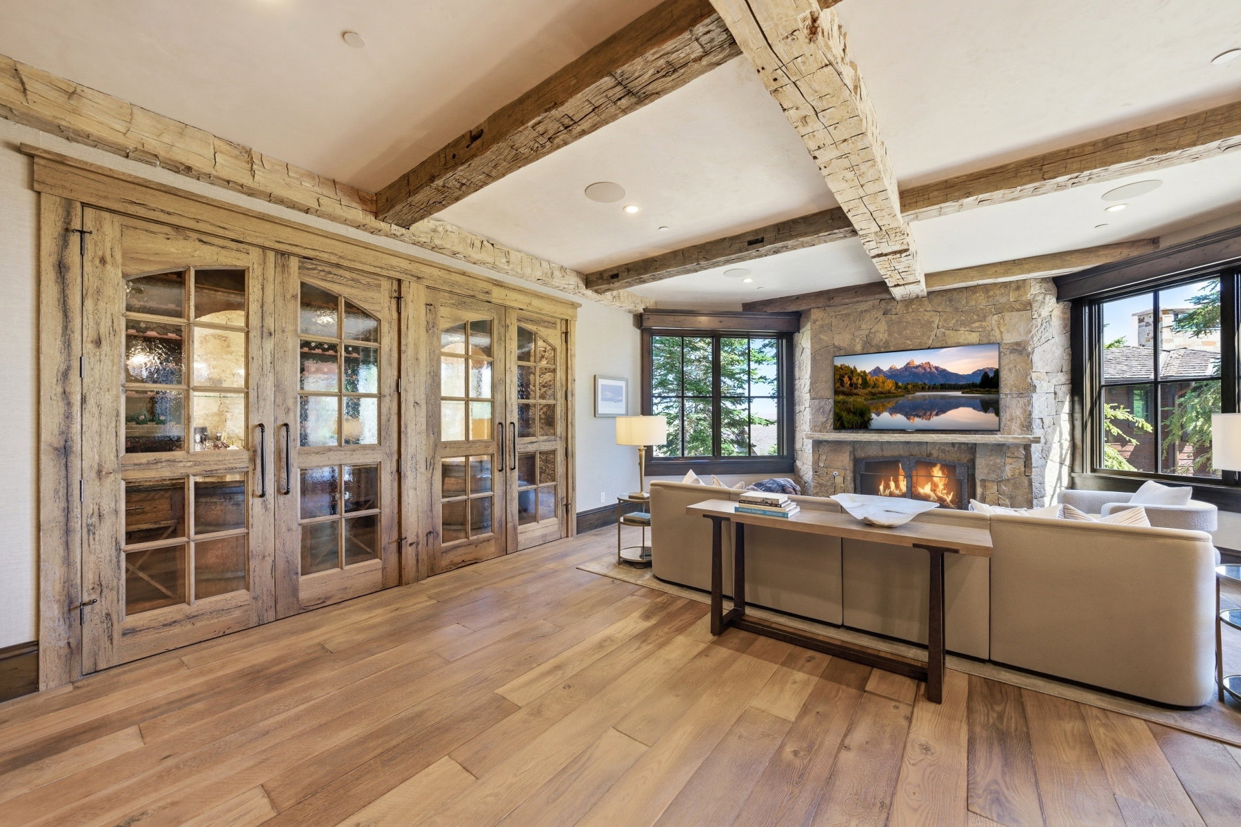 Living space with wide plank wood-finish flooring, exposed wood ceiling beams, and a stone-clad fireplace