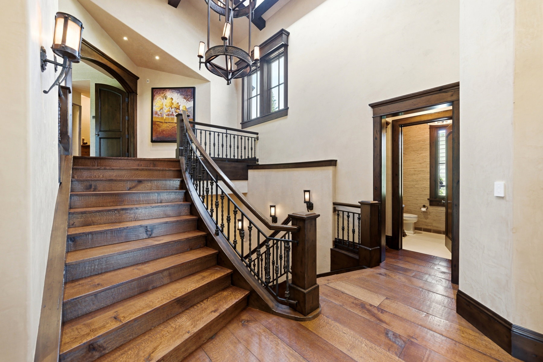 Grand wood-finish staircase with wrought iron railing, complemented by matching wood-finish flooring