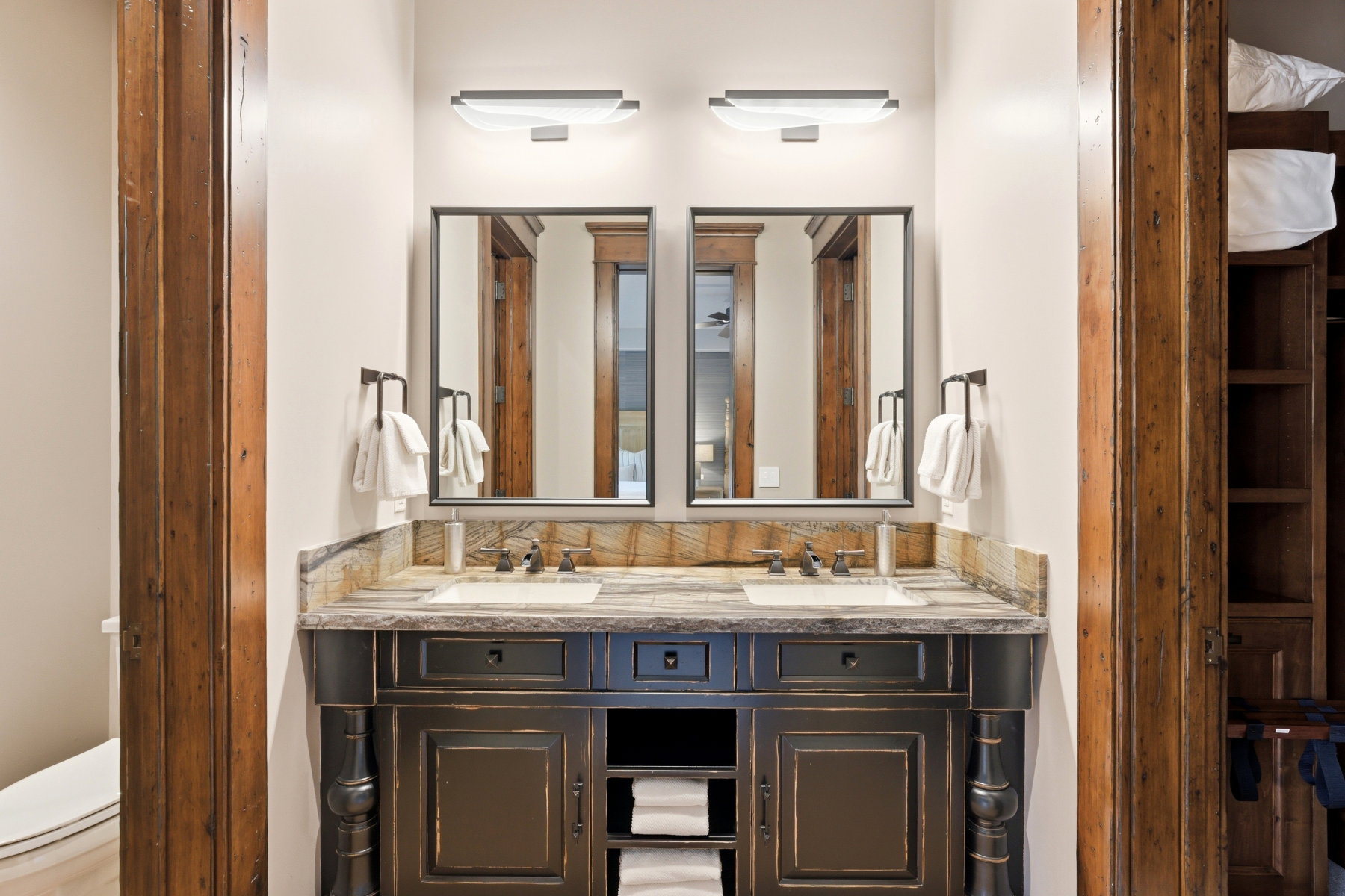 Distressed black wood-finish double vanity featuring dual integrated sinks, individual rectangular mirrors, and two wall-mounted light fixtures